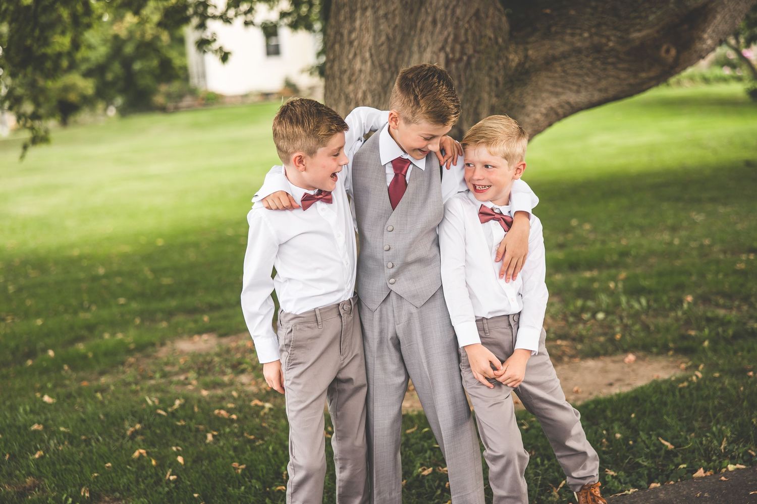 Three young boys in formal attire sharing a playful moment under a tree.
