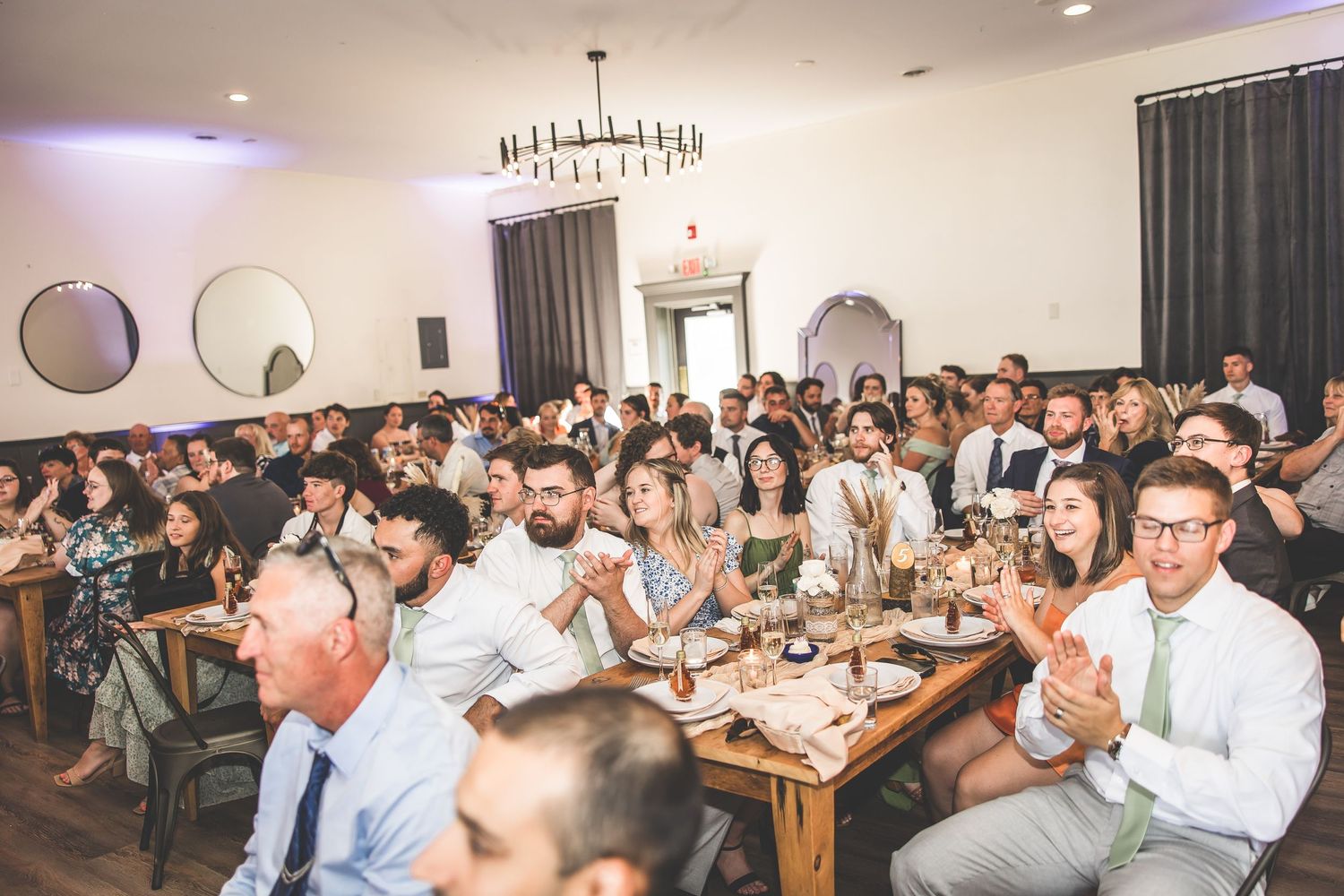 Wedding guests seated at long tables during indoor reception celebration.