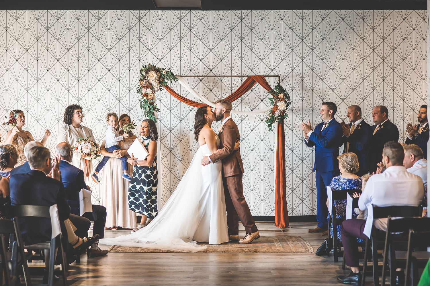 Wide view of wedding ceremony with guests seated and couple at decorated arch.
