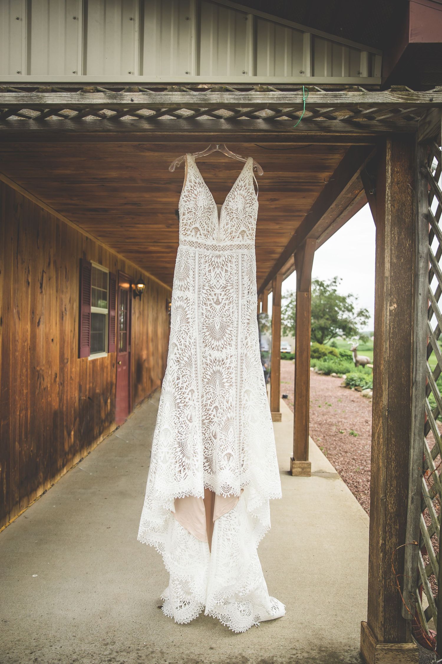 White lace wedding dress hanging in wooden covered walkway.