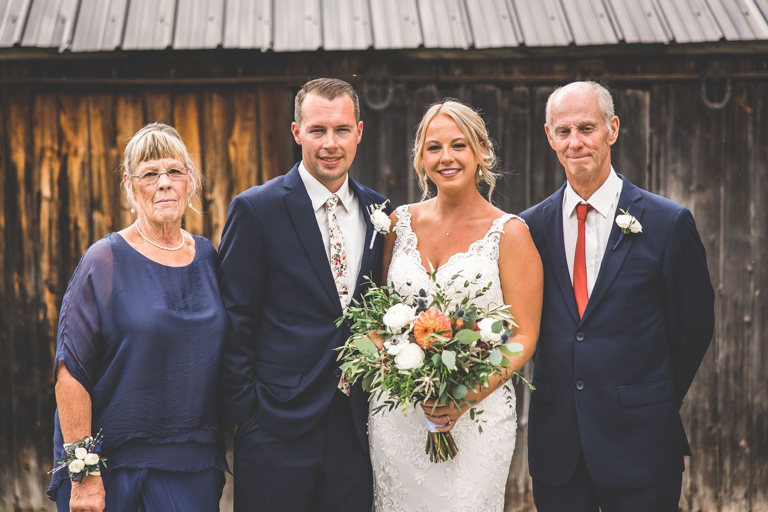 Wedding party members in navy and white attire pose together against rustic barn backdrop.