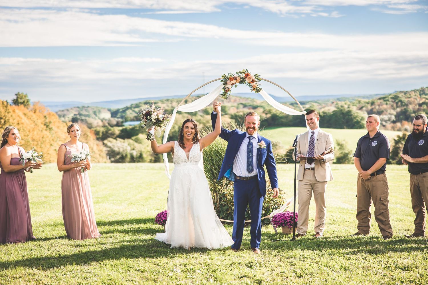 Panoramic view of wedding ceremony on hilltop with guests seated in white chairs.