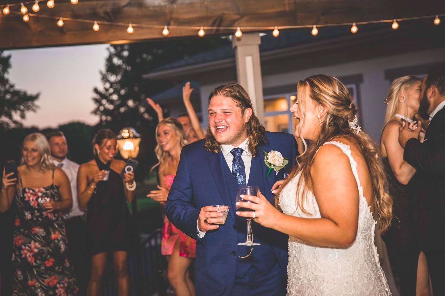 Wedding guests enjoying drinks and dancing during an outdoor evening celebration.