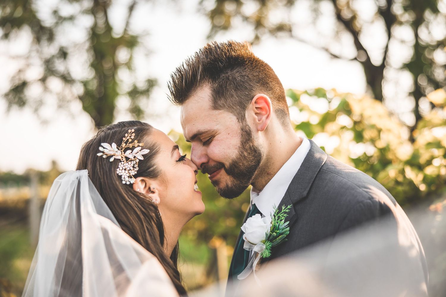 A romantic moment between newlyweds sharing a tender embrace at sunset with a delicate floral hair accessory.