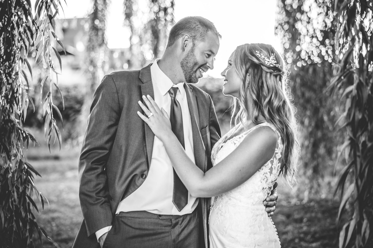 Black and white wedding photo showing tender moment under weeping willow branches.