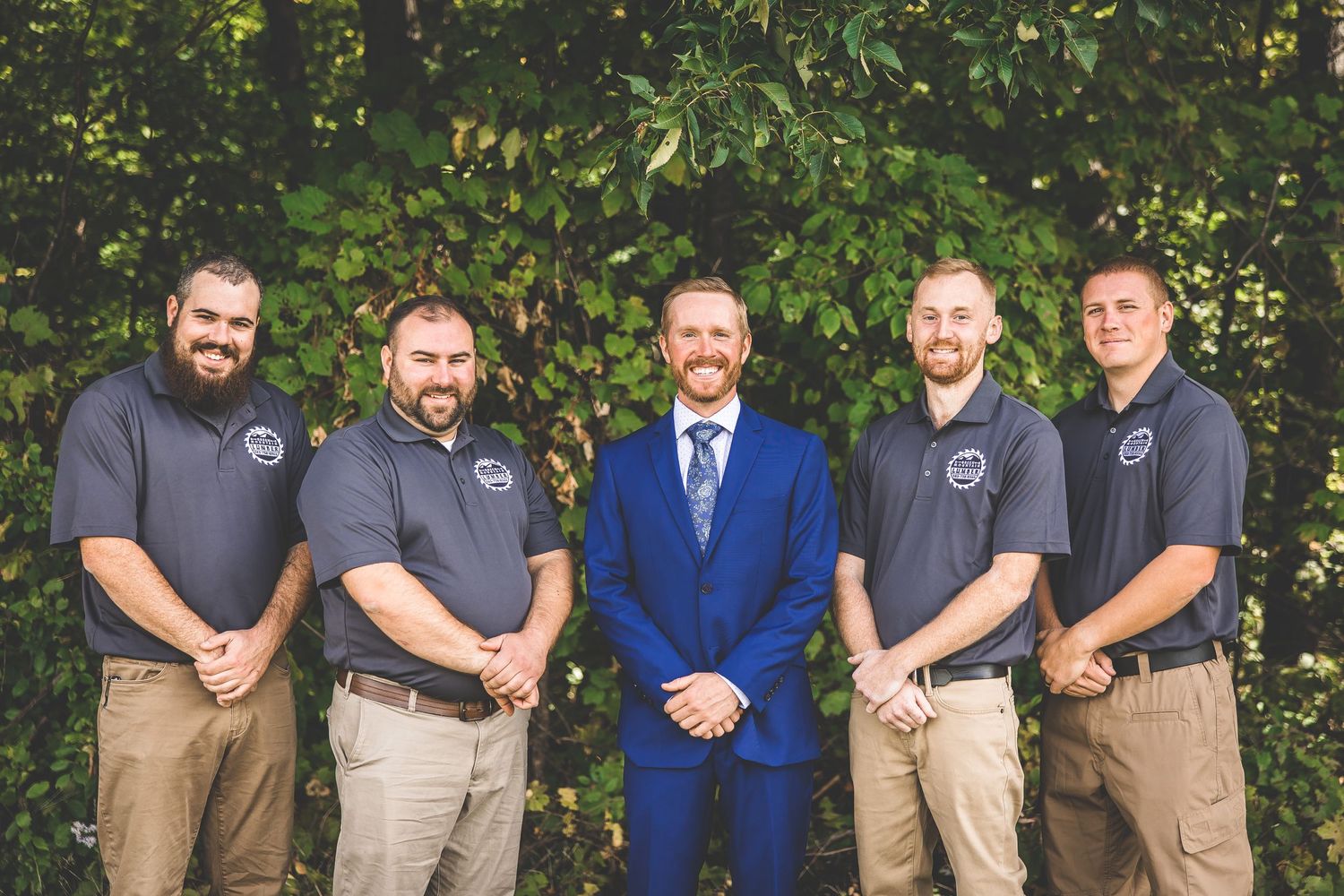 Groomsmen in casual attire and one in blue suit pose together outdoors.