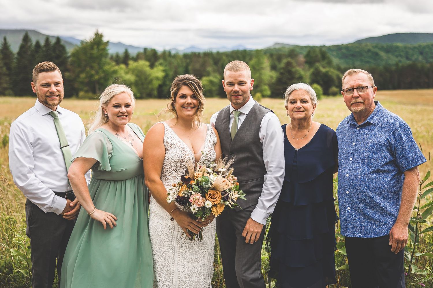 Wedding party members gather for photos in a sunny mountain field.
