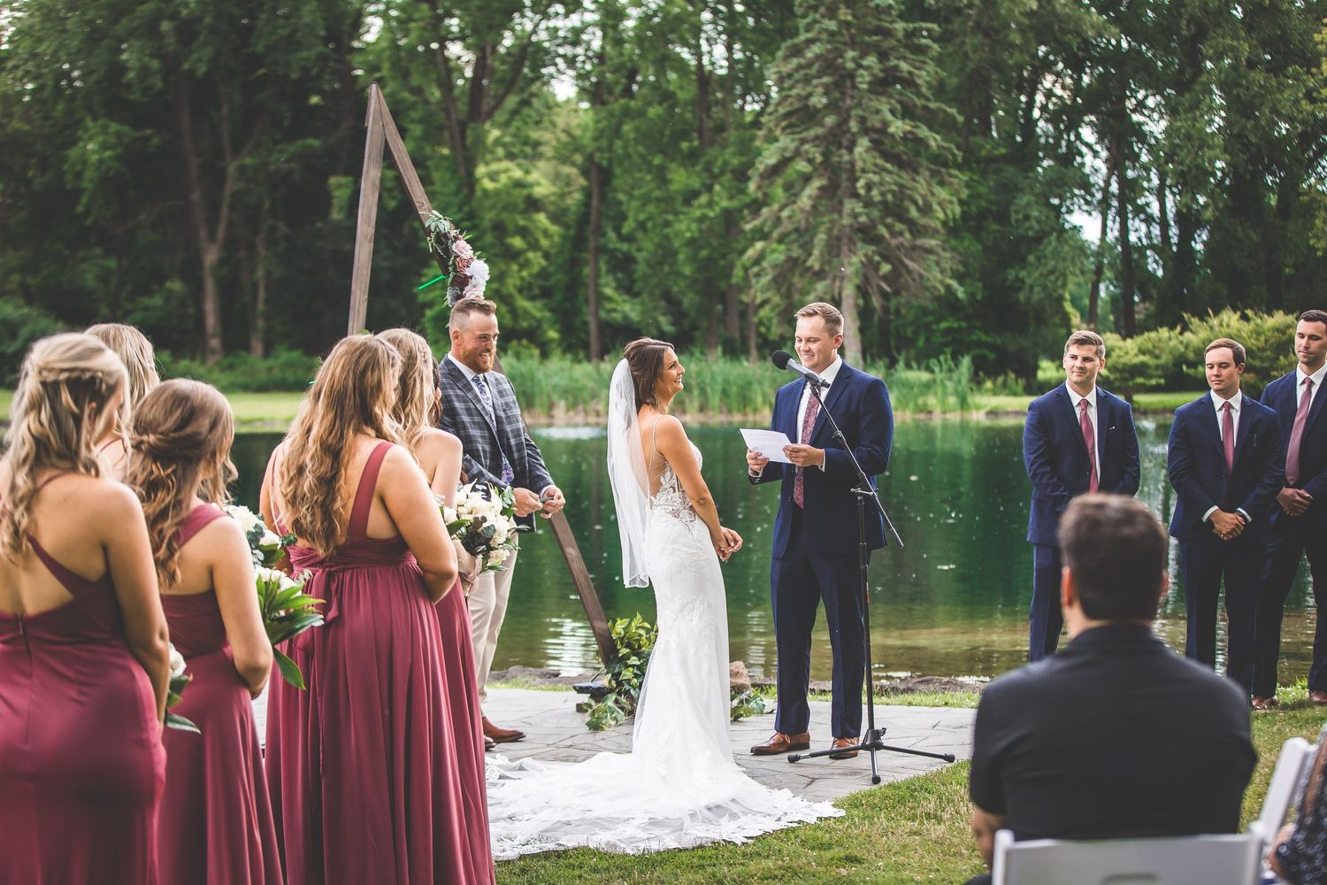 Wedding party lined up during outdoor ceremony with forest backdrop and burgundy bridesmaid dresses.