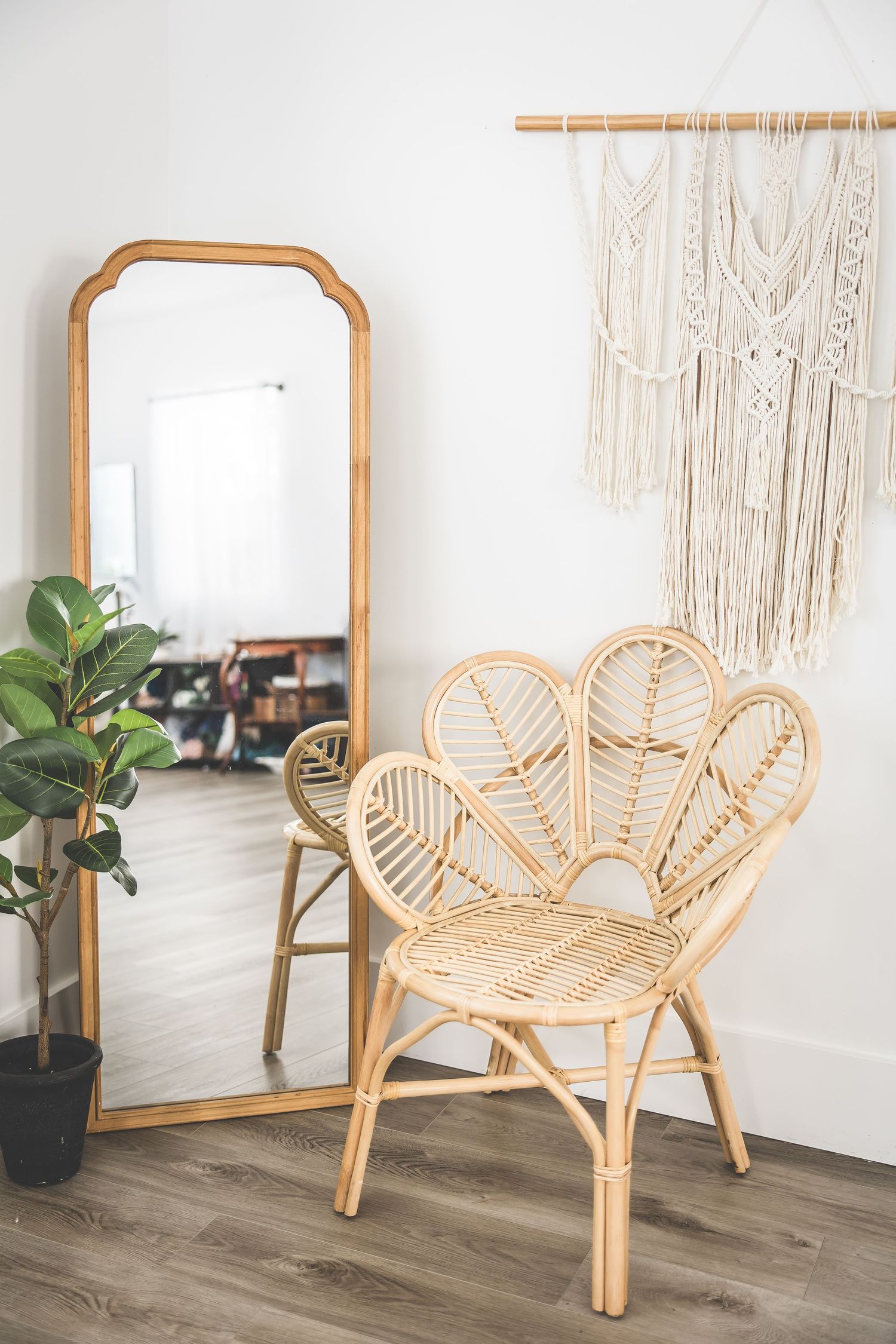 Rattan butterfly chair with curved design sits elegantly against white wall with macrame hangings and mirror.