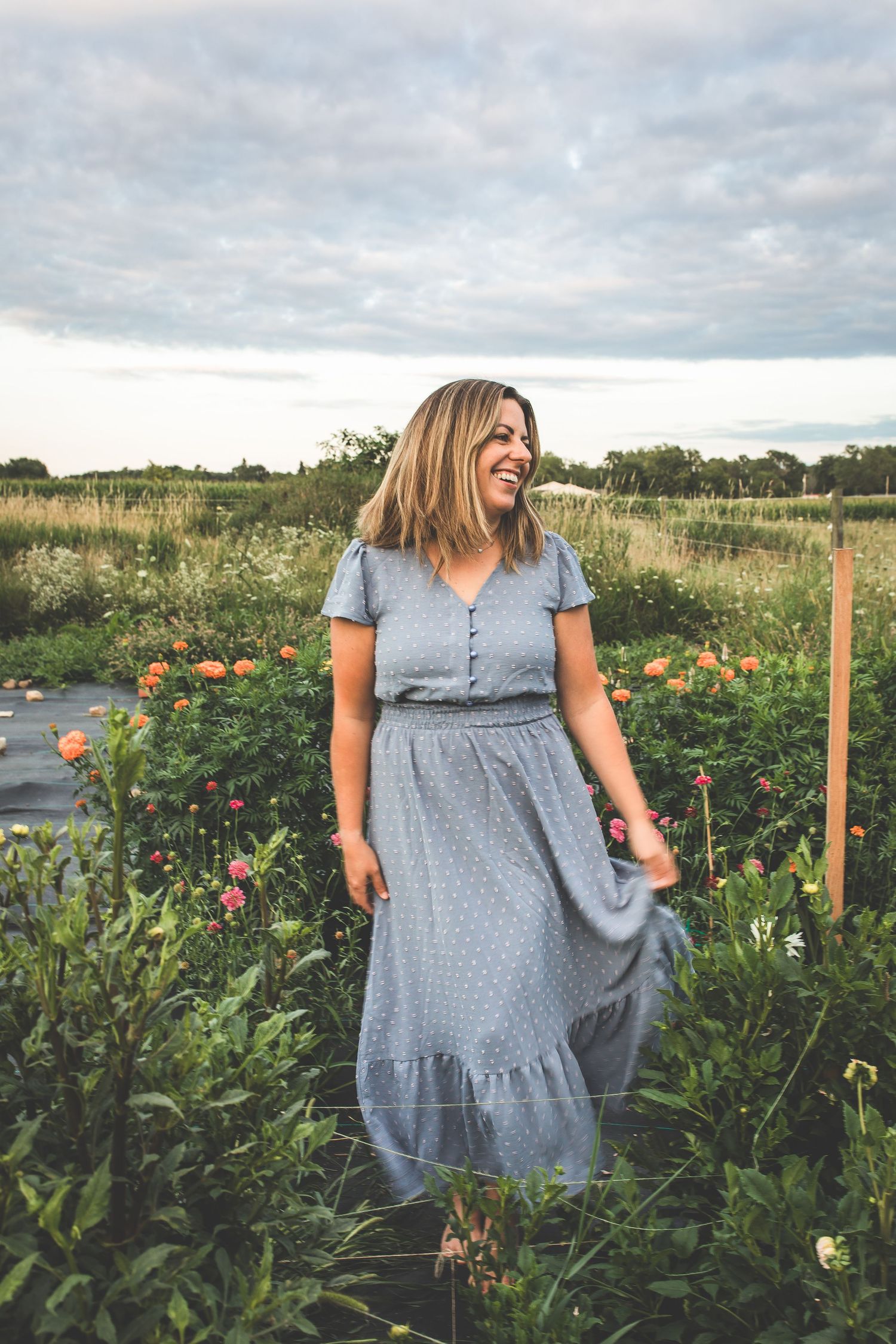 Woman in blue dress twirls through flower garden during golden hour photo session.