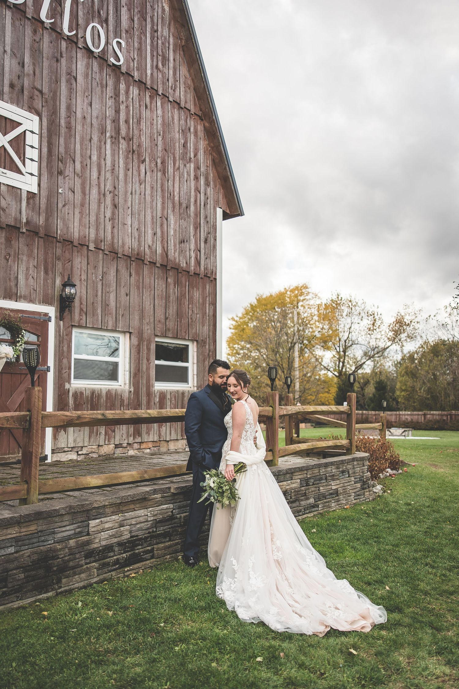 A rustic barn wedding photoshoot with weathered wood siding and stone foundation on an autumn day.