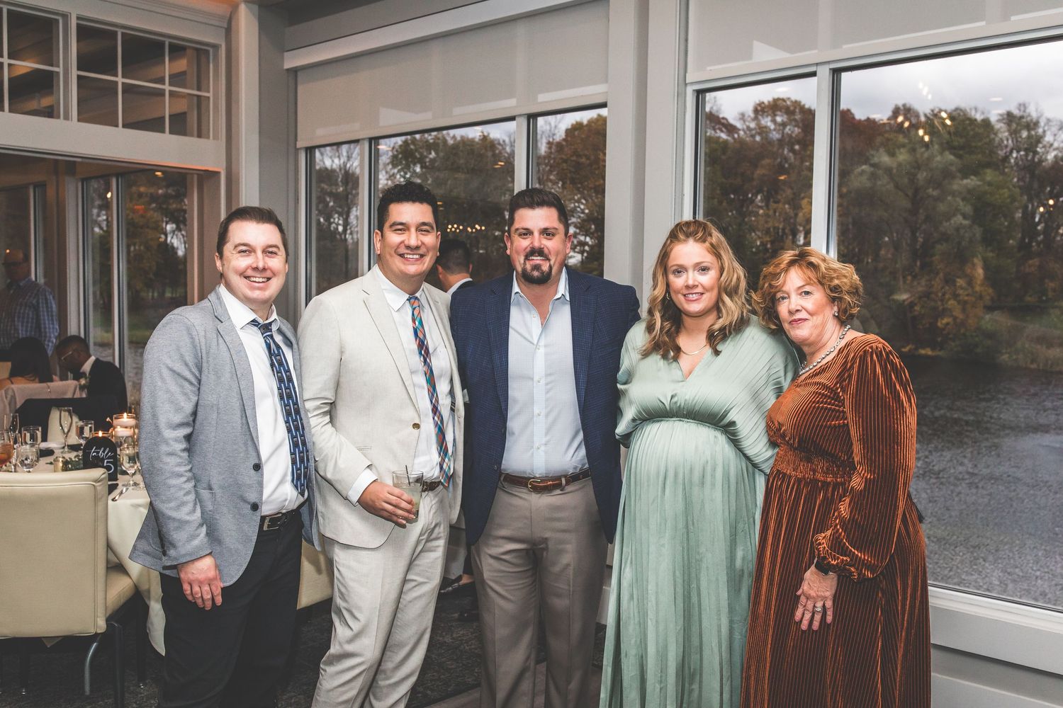 Wedding party poses together indoors near large windows overlooking water.