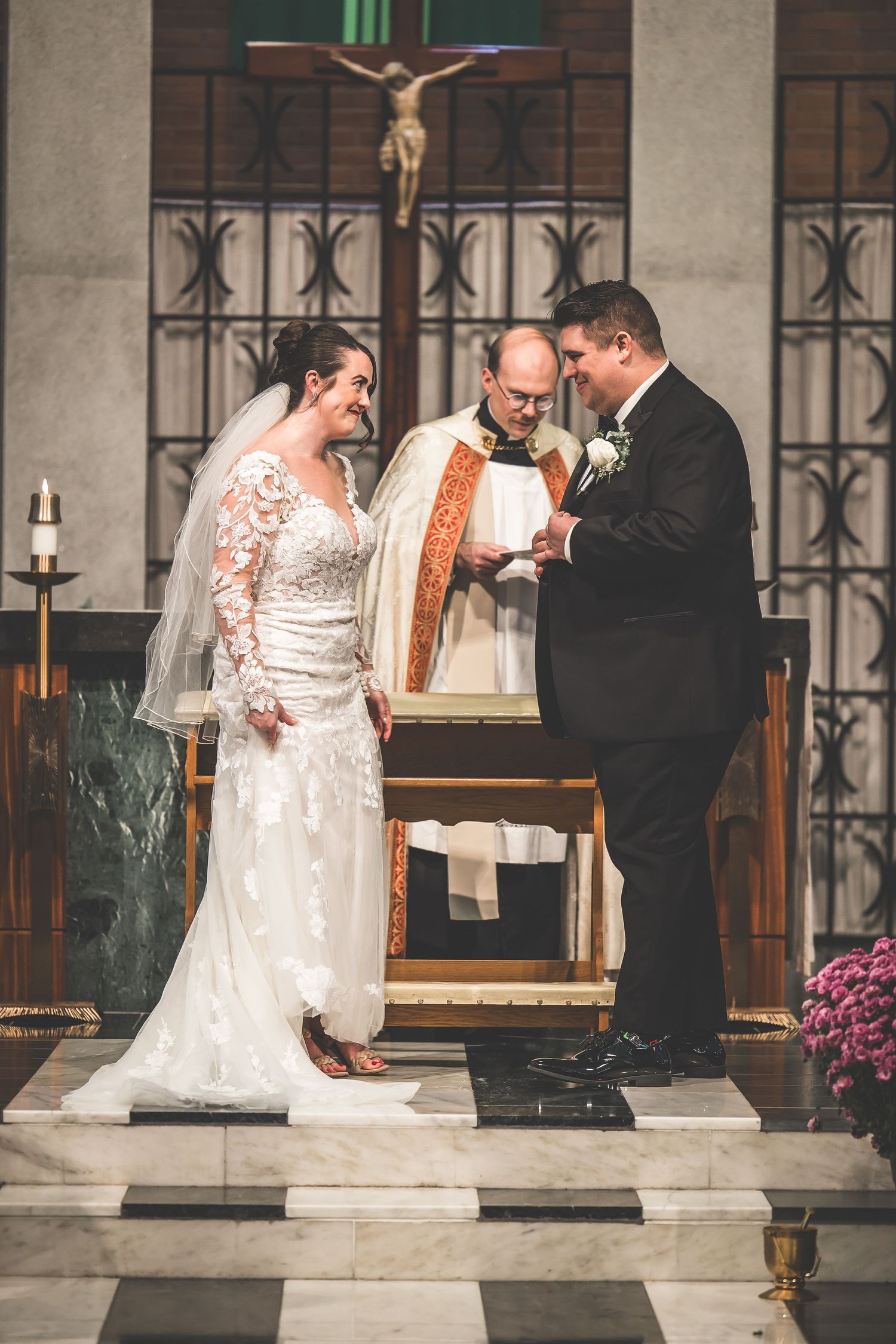 Wedding ceremony taking place in a beautiful brick church with ornate iron railings and green columns.