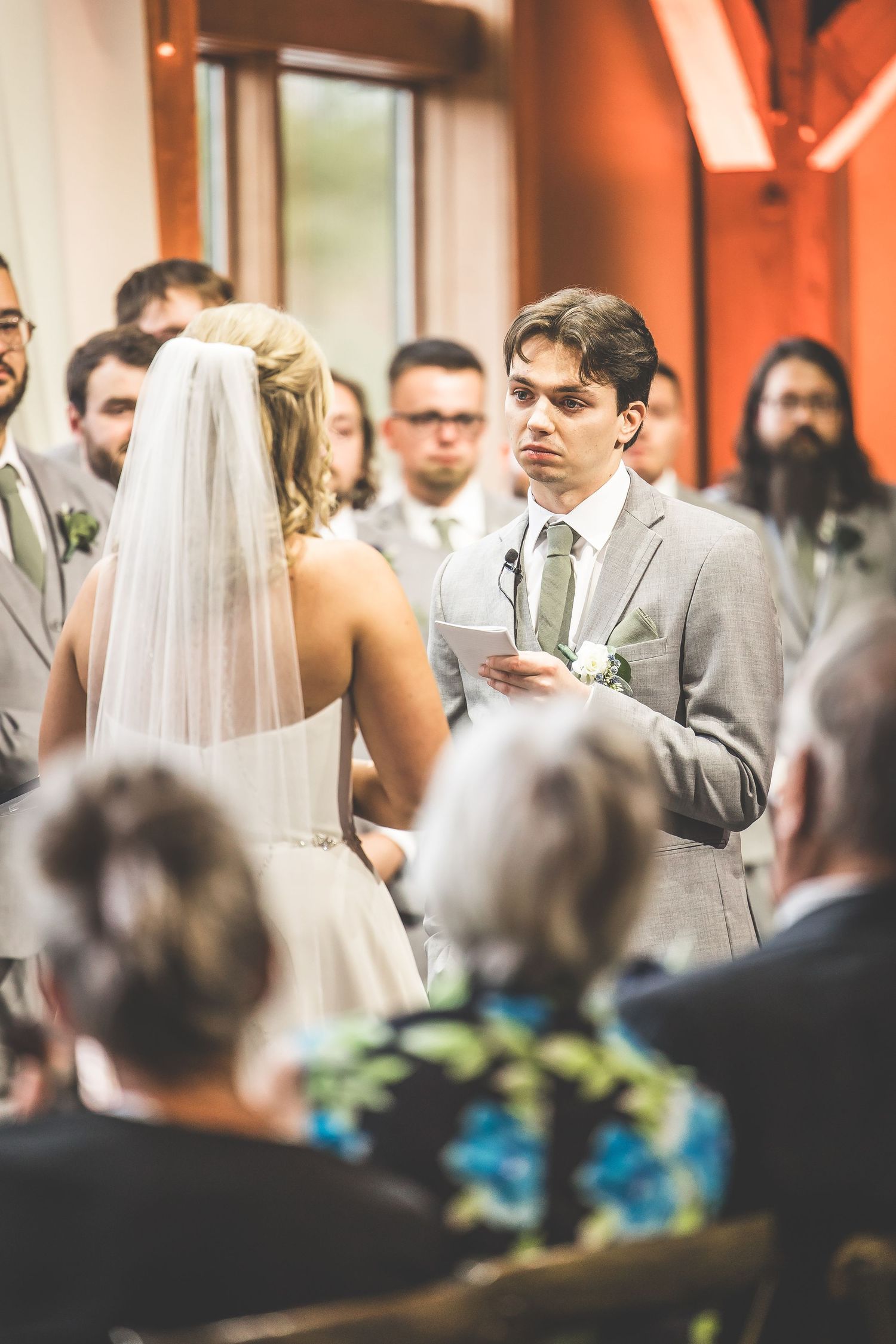 Wedding guests observe a ceremony from their seats as natural light streams through windows.