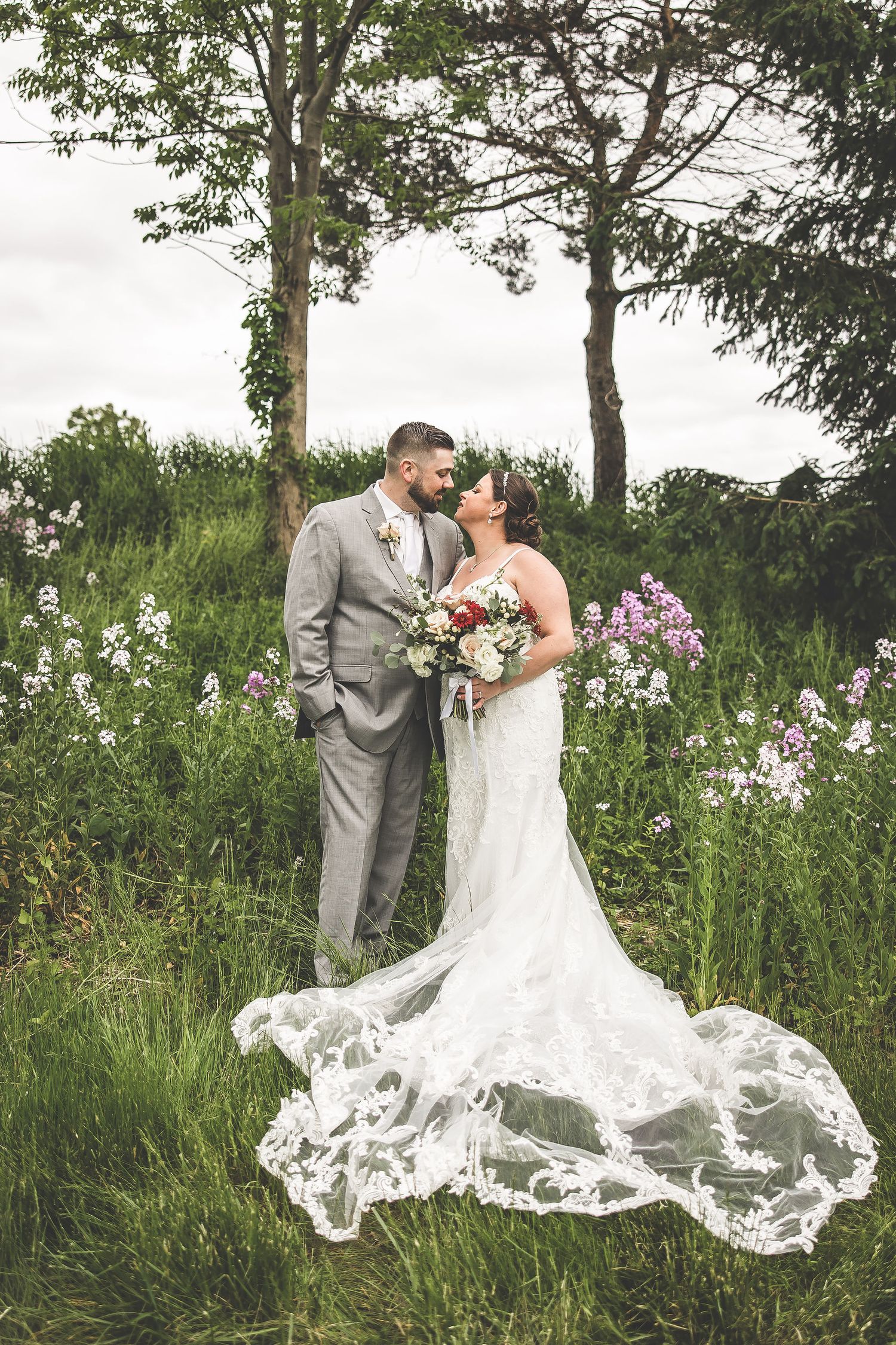 A romantic wedding portrait in a wildflower field with the bride's lace train elegantly spread on the ground.