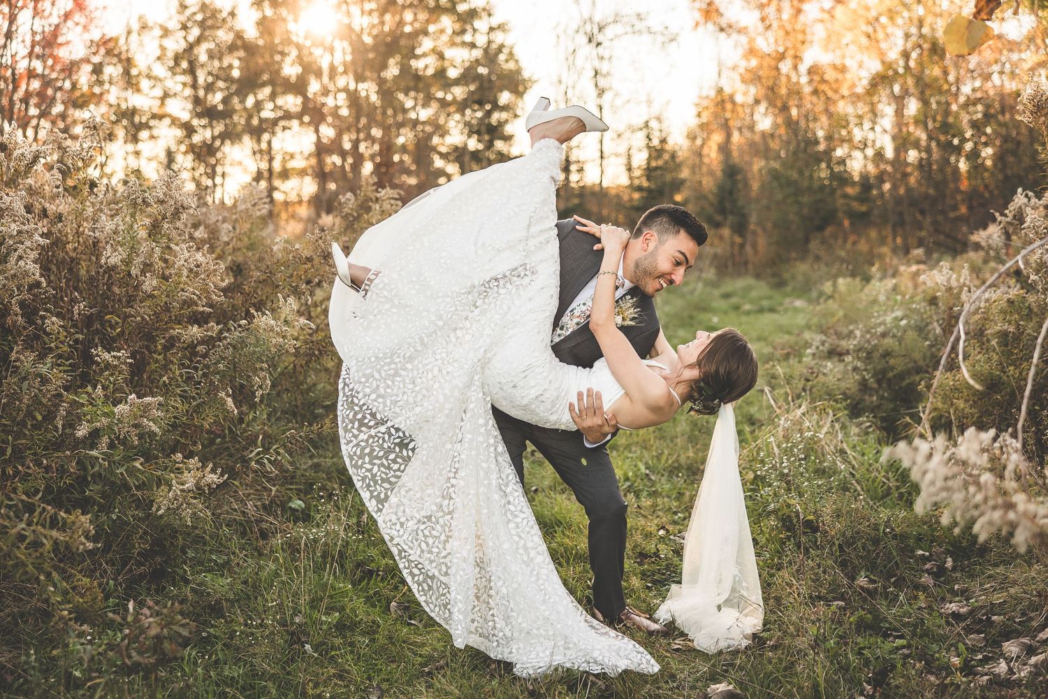 Wedding couple poses playfully in a natural outdoor setting during golden hour.