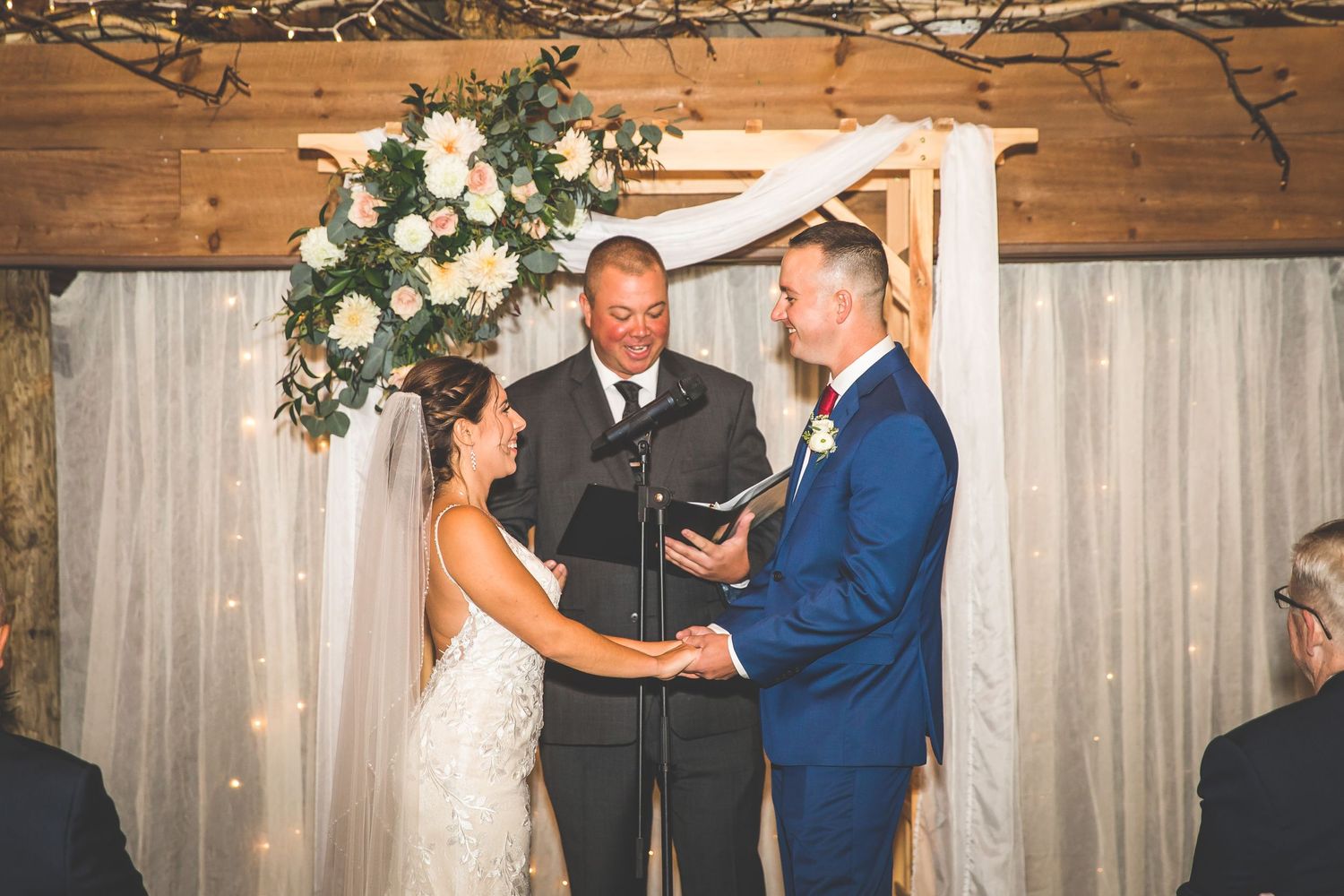 Wedding ceremony taking place in rustic barn venue with elegant floral arrangements.