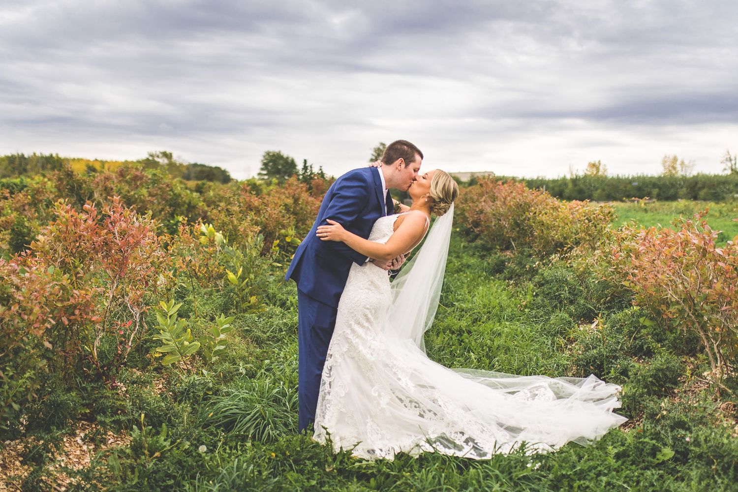 Wedding couple poses for romantic portraits in field with dramatic flowing veil.