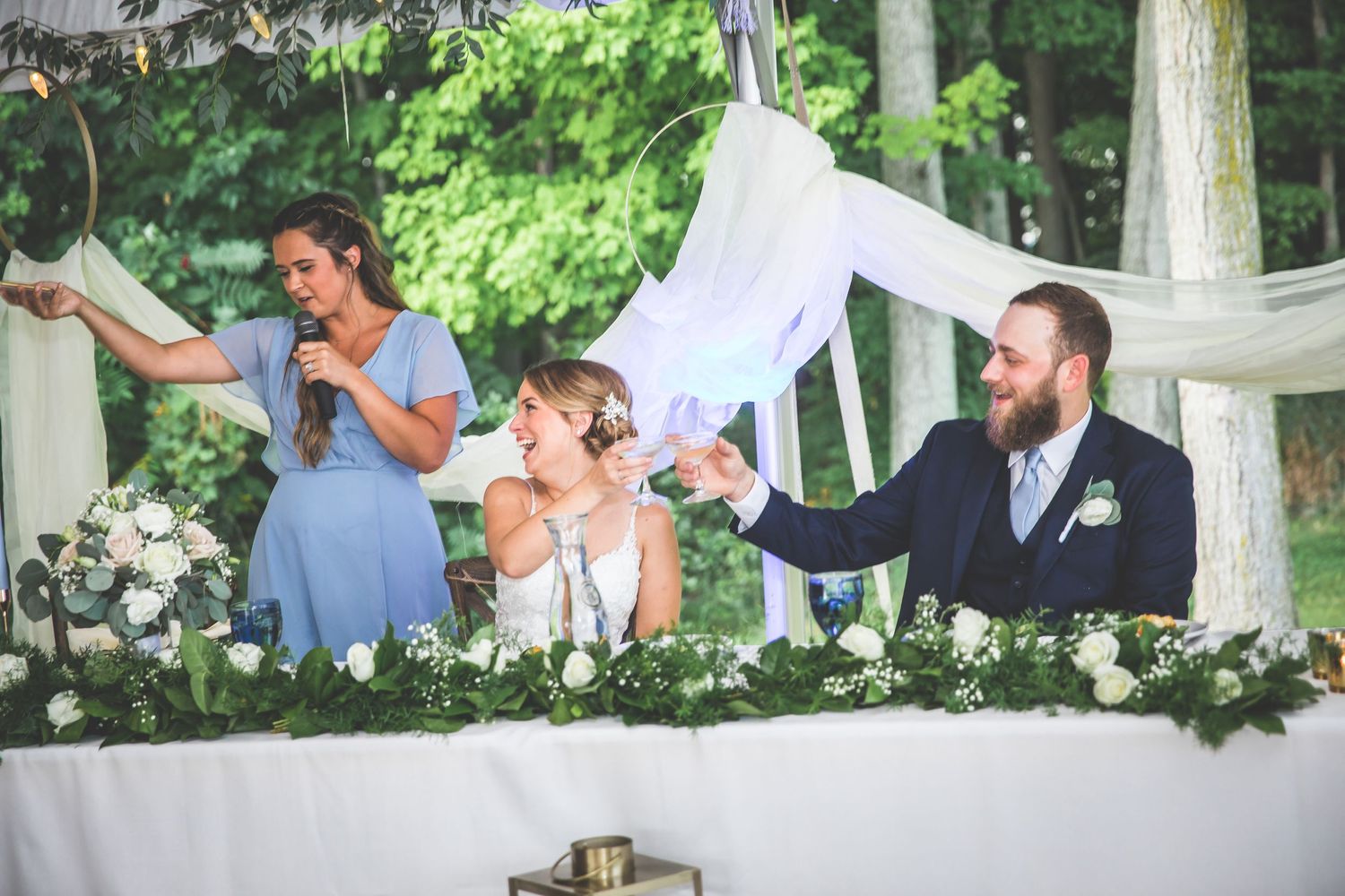Wedding party celebrating with dance moves under a garden tent surrounded by lush greenery.