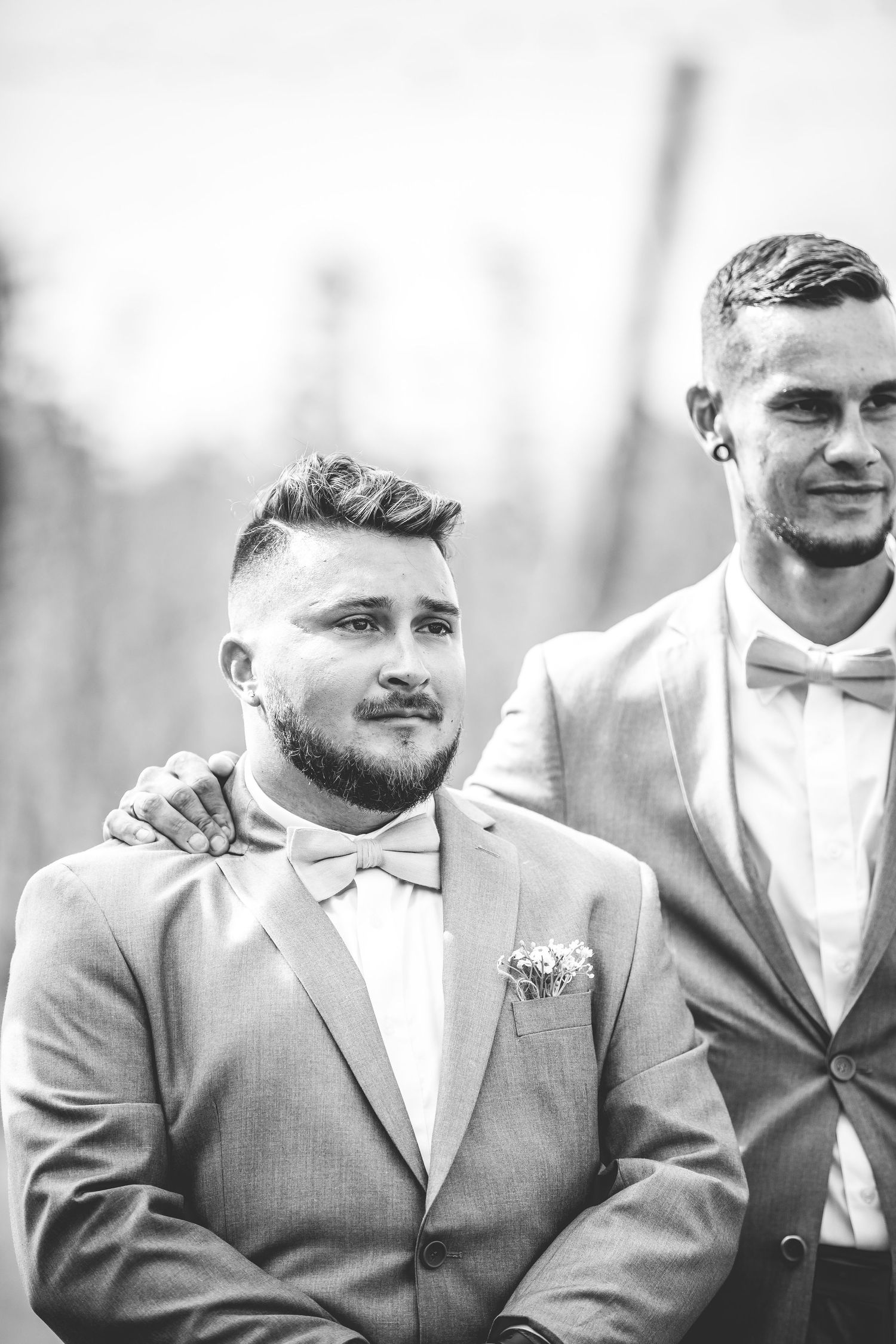 Groomsmen in light gray suits and bowties stand together in black and white photo.