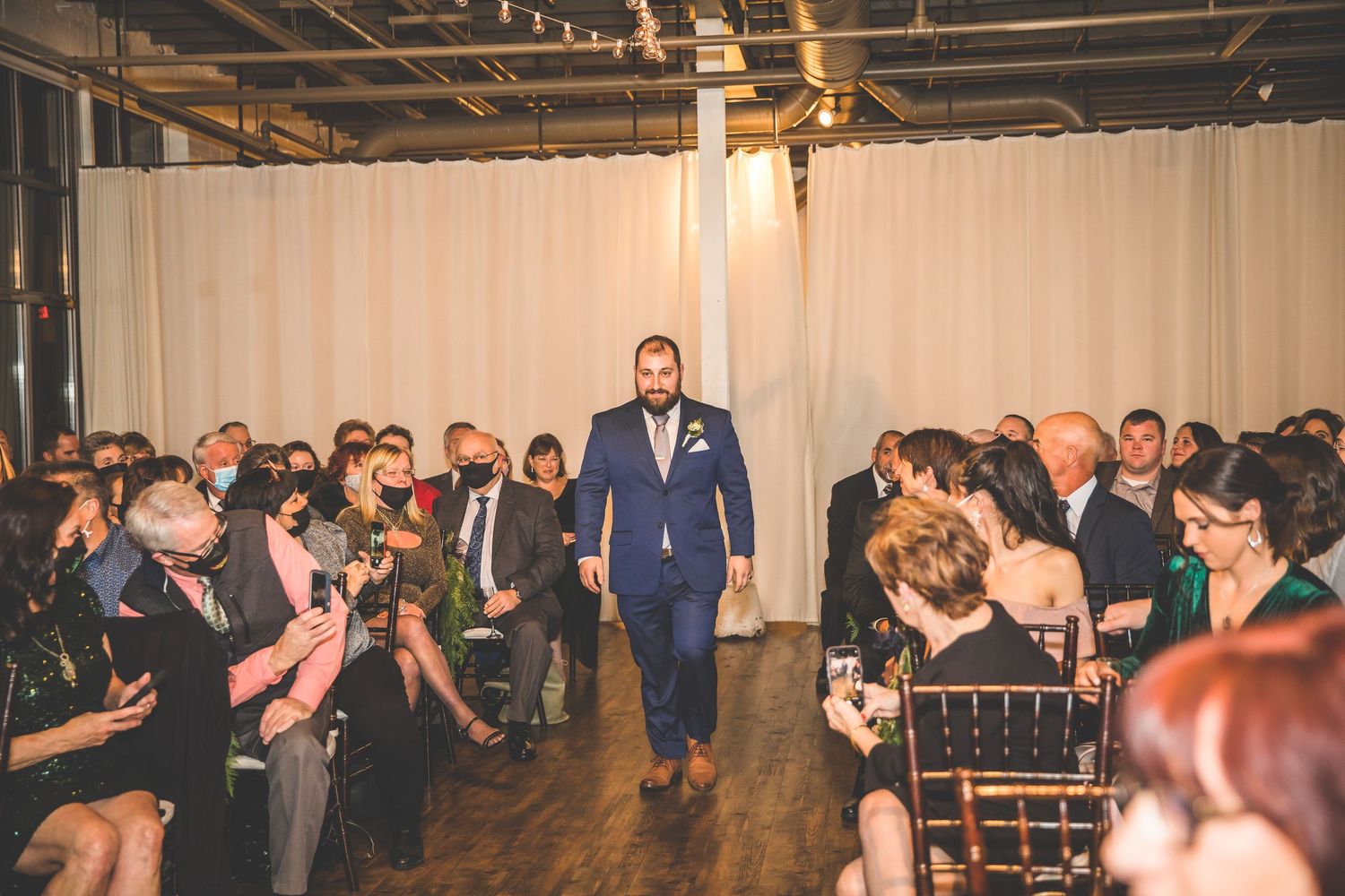 Wedding ceremony aisle with guests seated on either side in industrial-style venue.