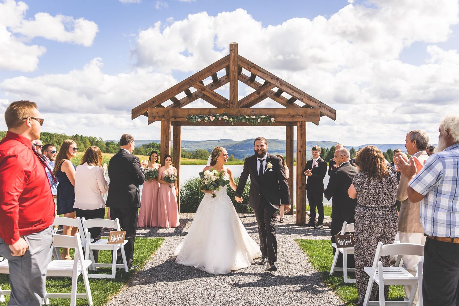 Guests celebrate at an outdoor wedding ceremony under a timber-framed pavilion with mountain views.