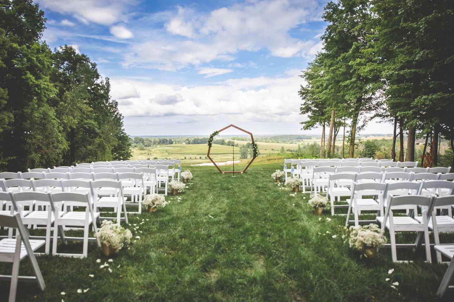 White chairs set up for outdoor wedding ceremony with trees in background.