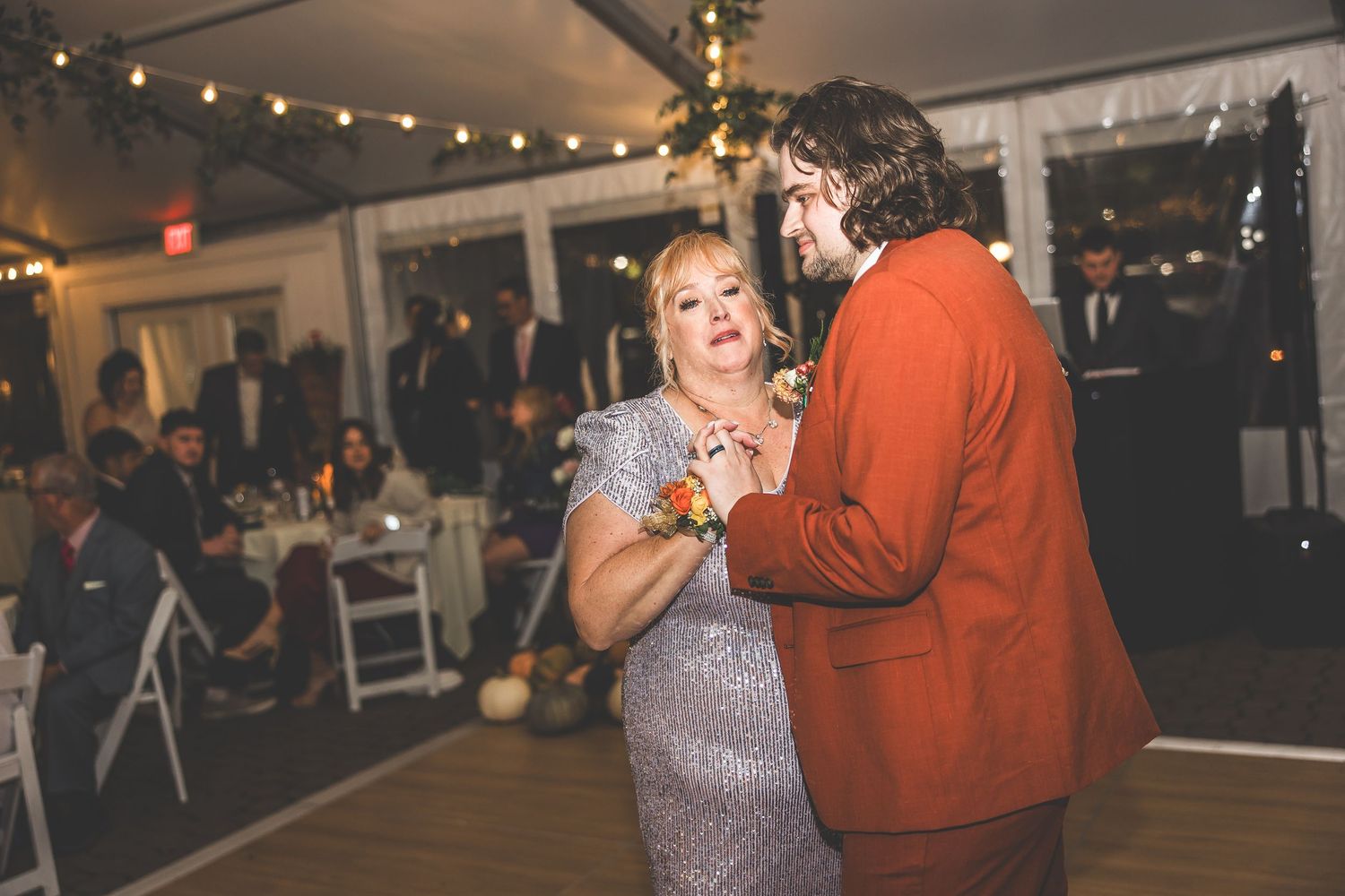 Wedding celebration under string lights with guests dancing in formal attire.