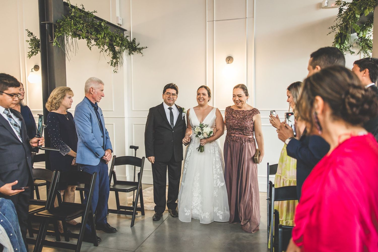 Wedding party members interact casually during reception in elegant white-walled venue.