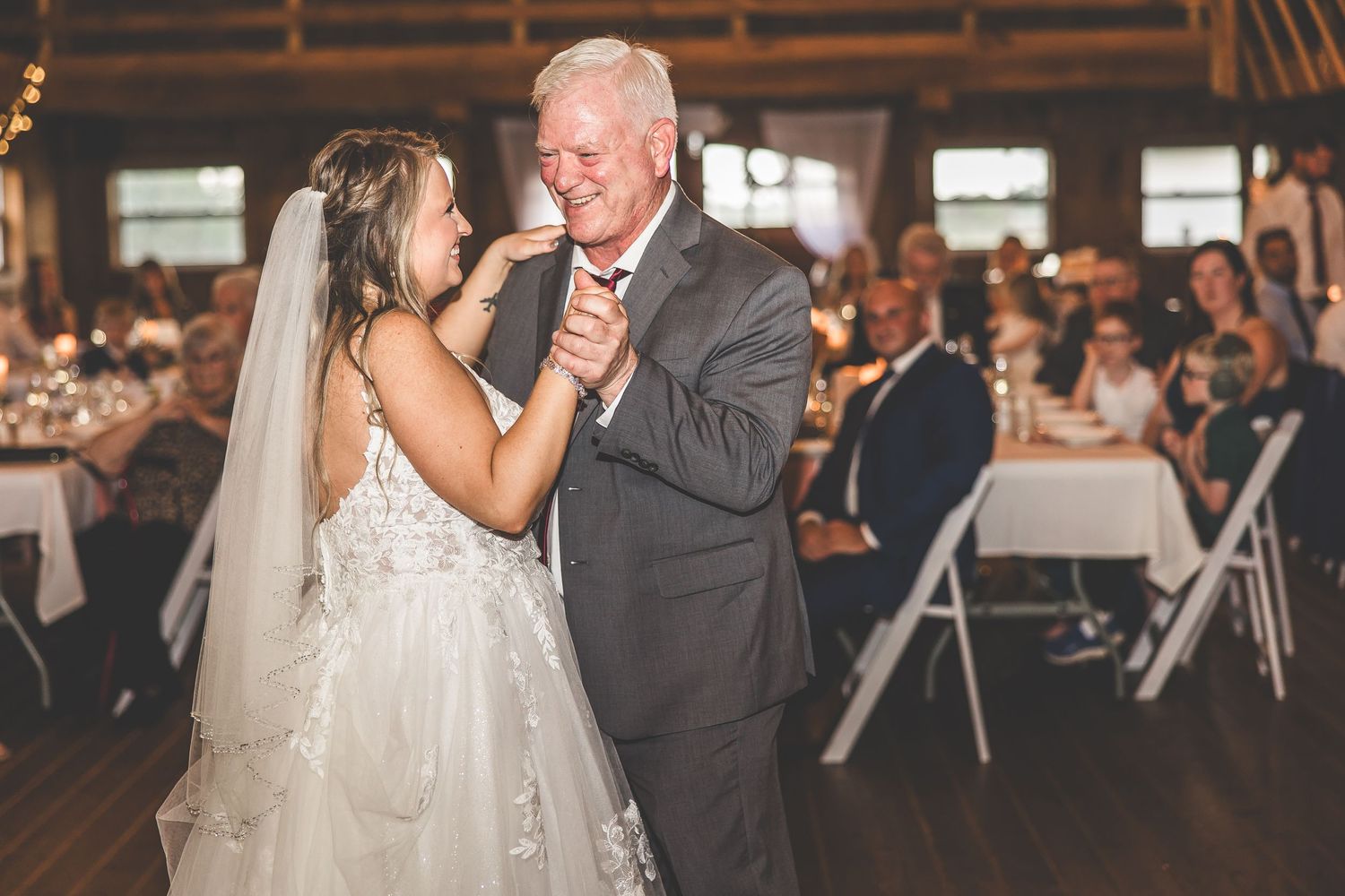 Wedding dance in progress at rustic barn venue with wooden walls and elegant chandeliers.