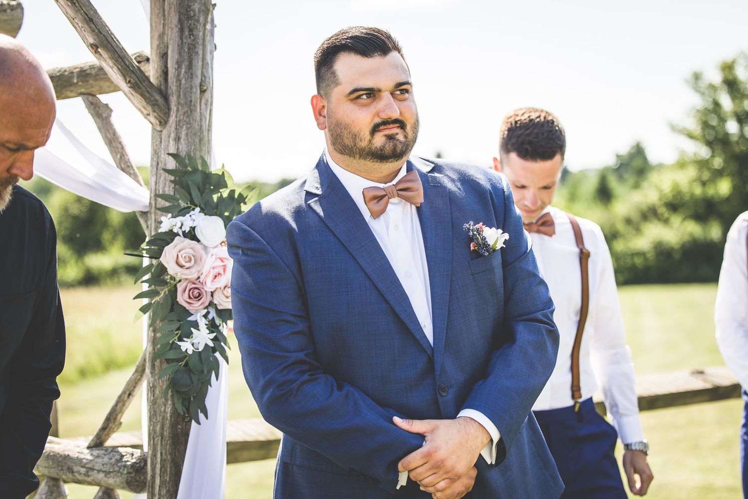 Wedding party members in navy suits and formal attire pose outdoors on a sunny day.