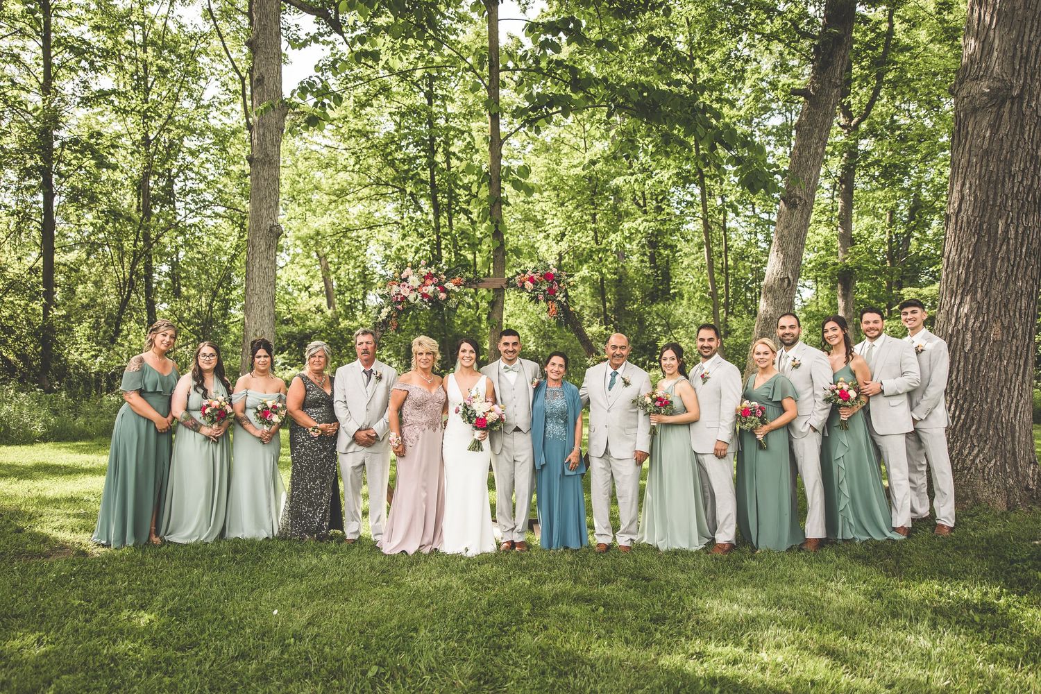 Large wedding party group photo with bridesmaids in pastel dresses and groomsmen in light suits.