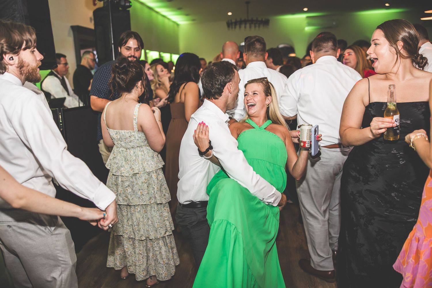 Wedding guests dancing and celebrating in a venue with green lighting accents.