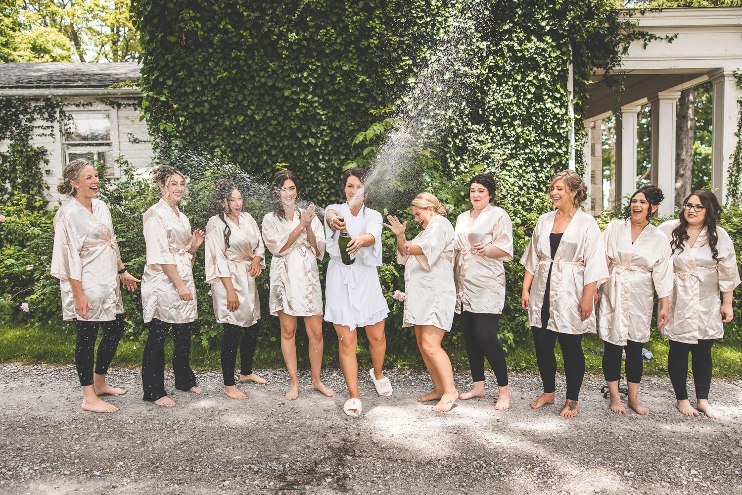 Wedding party lined up in white attire for a fun group photo outdoors.