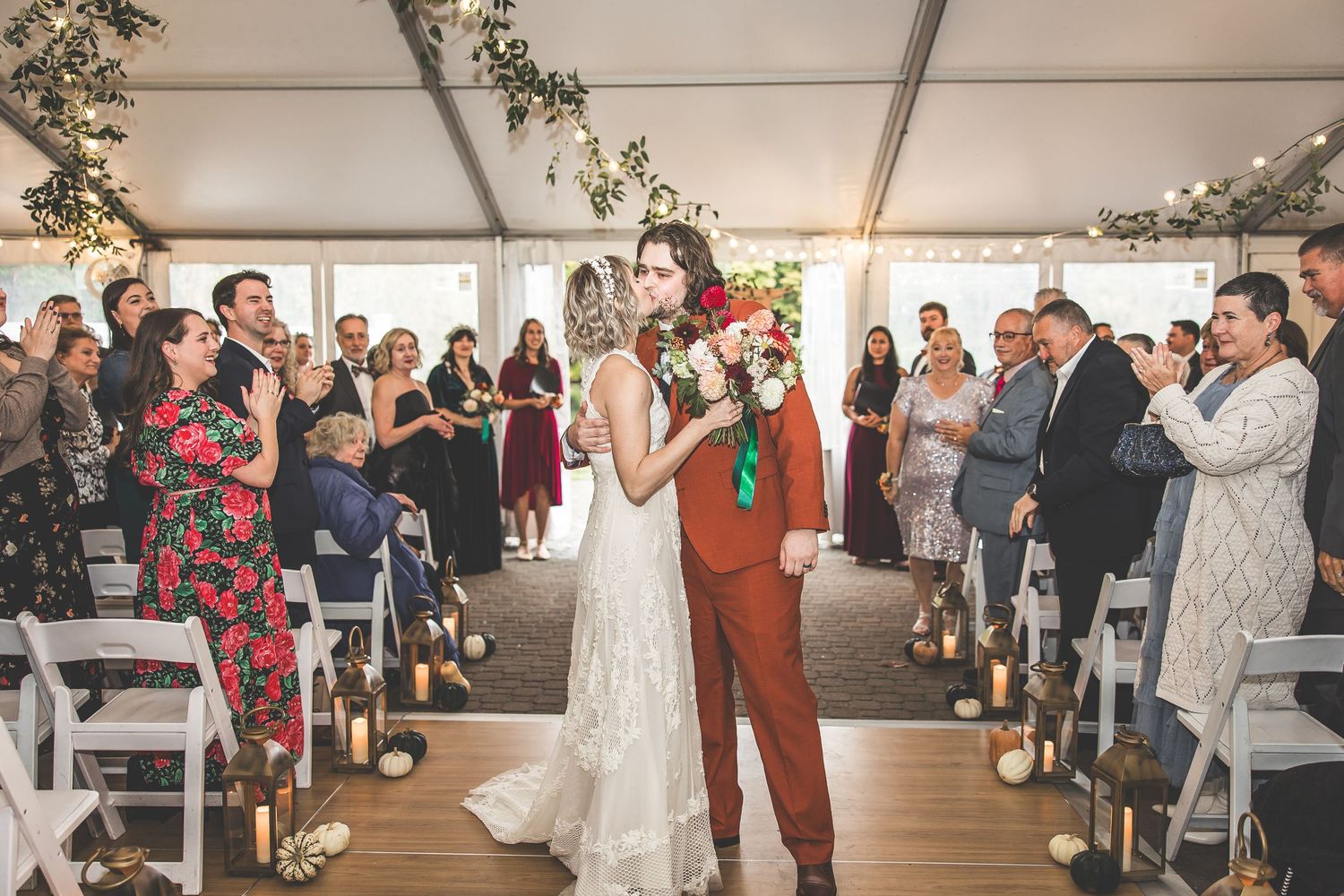 Wedding guests gathered in tent venue with elegant lighting and floral arrangements.