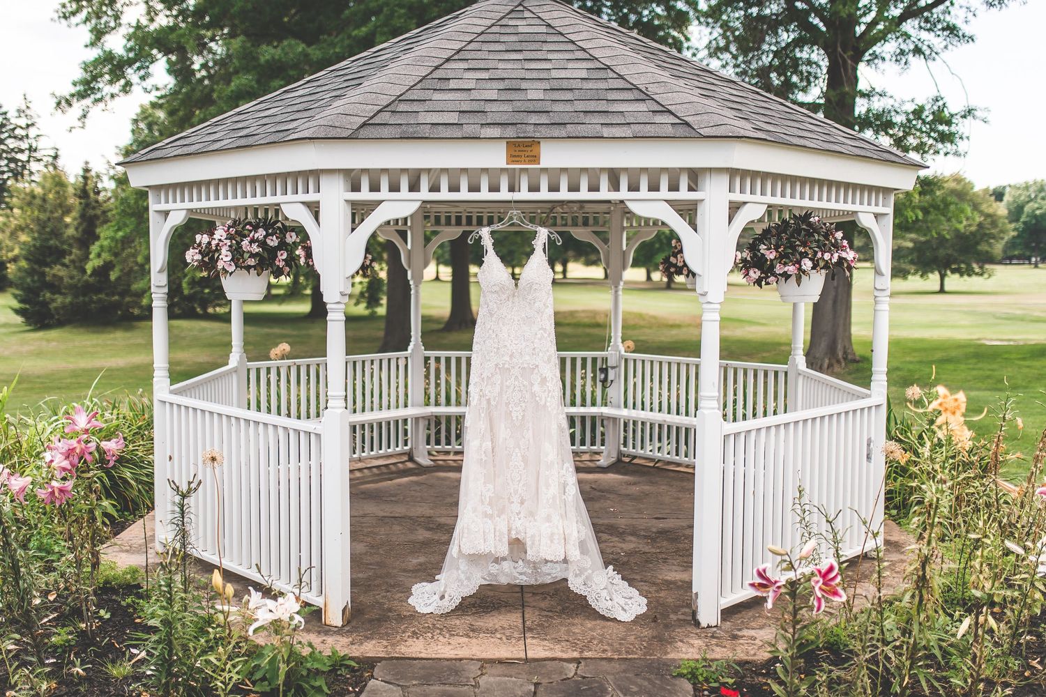 White wedding dress hanging in a garden gazebo decorated with purple flowers.