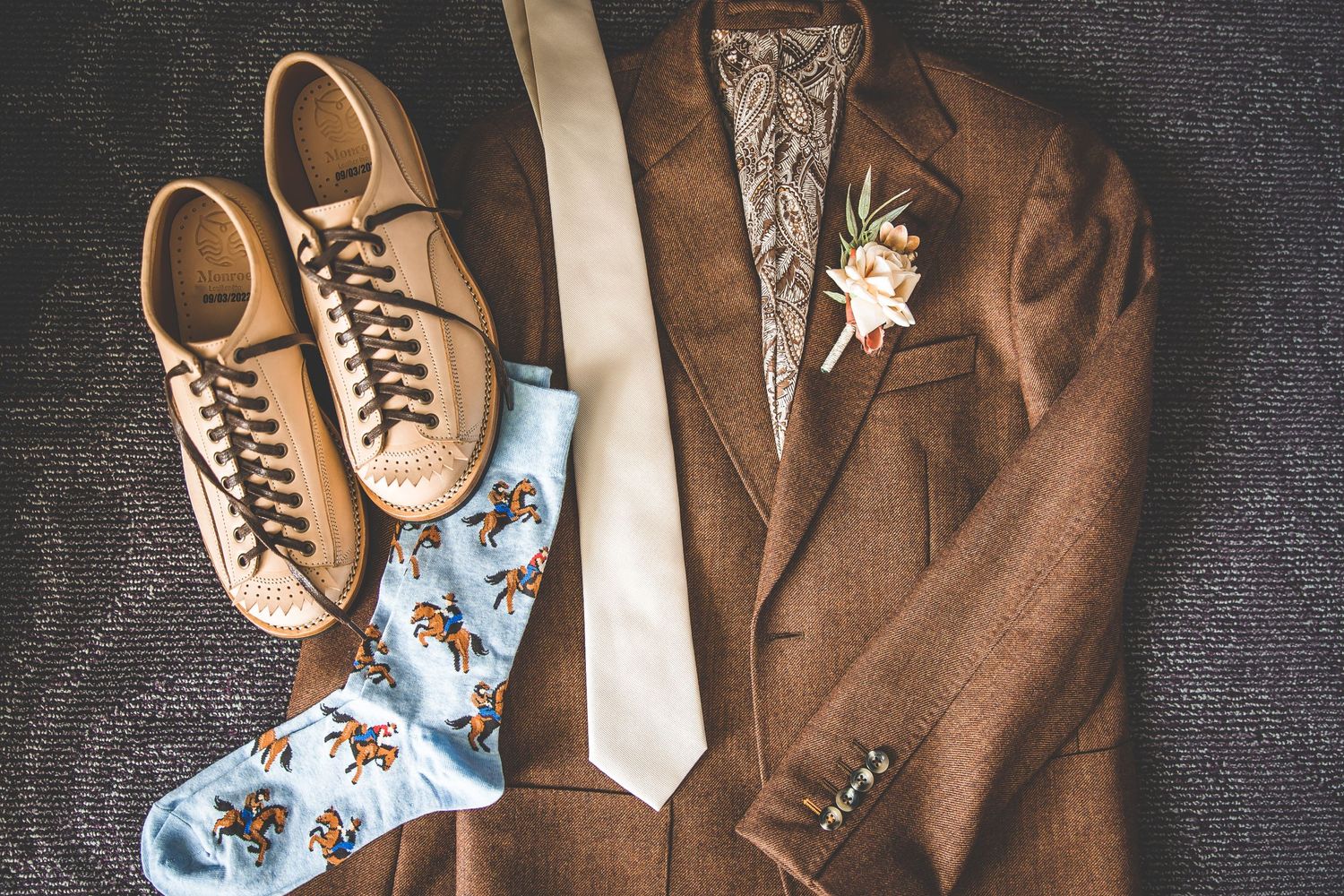 Brown suit, tie and dress shoes laid out with blue patterned socks.