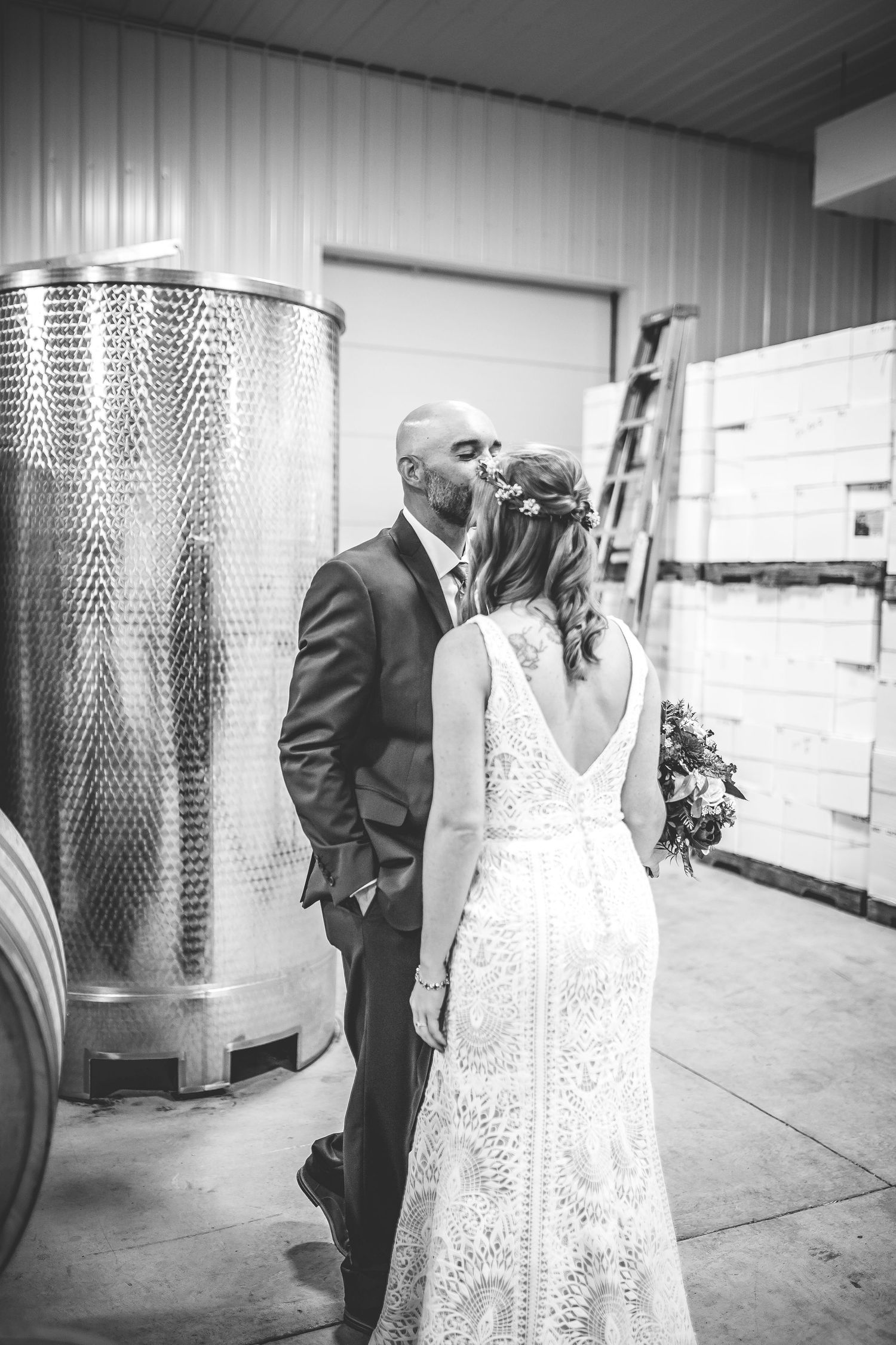 Black and white photo of a couple posing between large wine fermentation tanks.