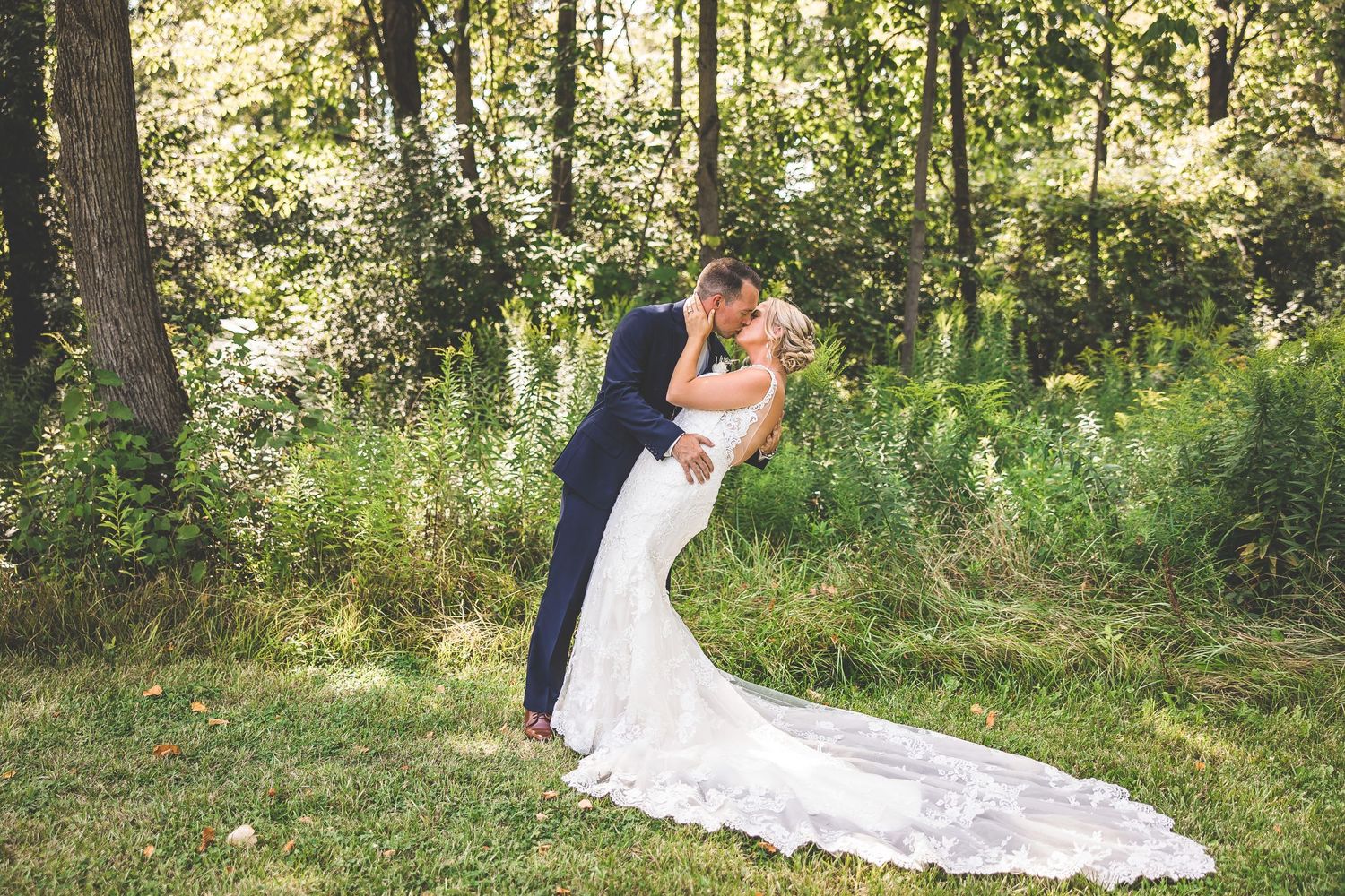 A romantic wedding photo showing a couple in an intimate embrace against a wooded backdrop.