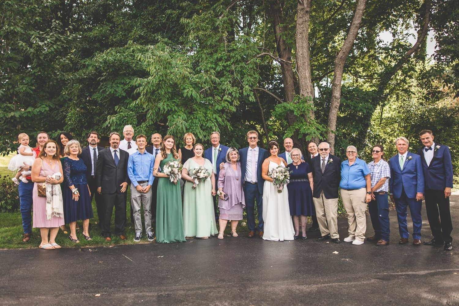 Large wedding party poses for formal group portraits in a garden setting.