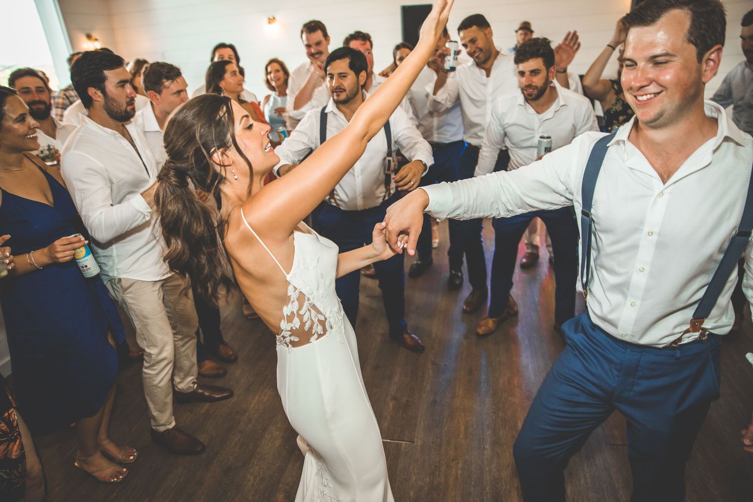 Wedding celebration on dance floor with guests dancing and celebrating in formal attire.