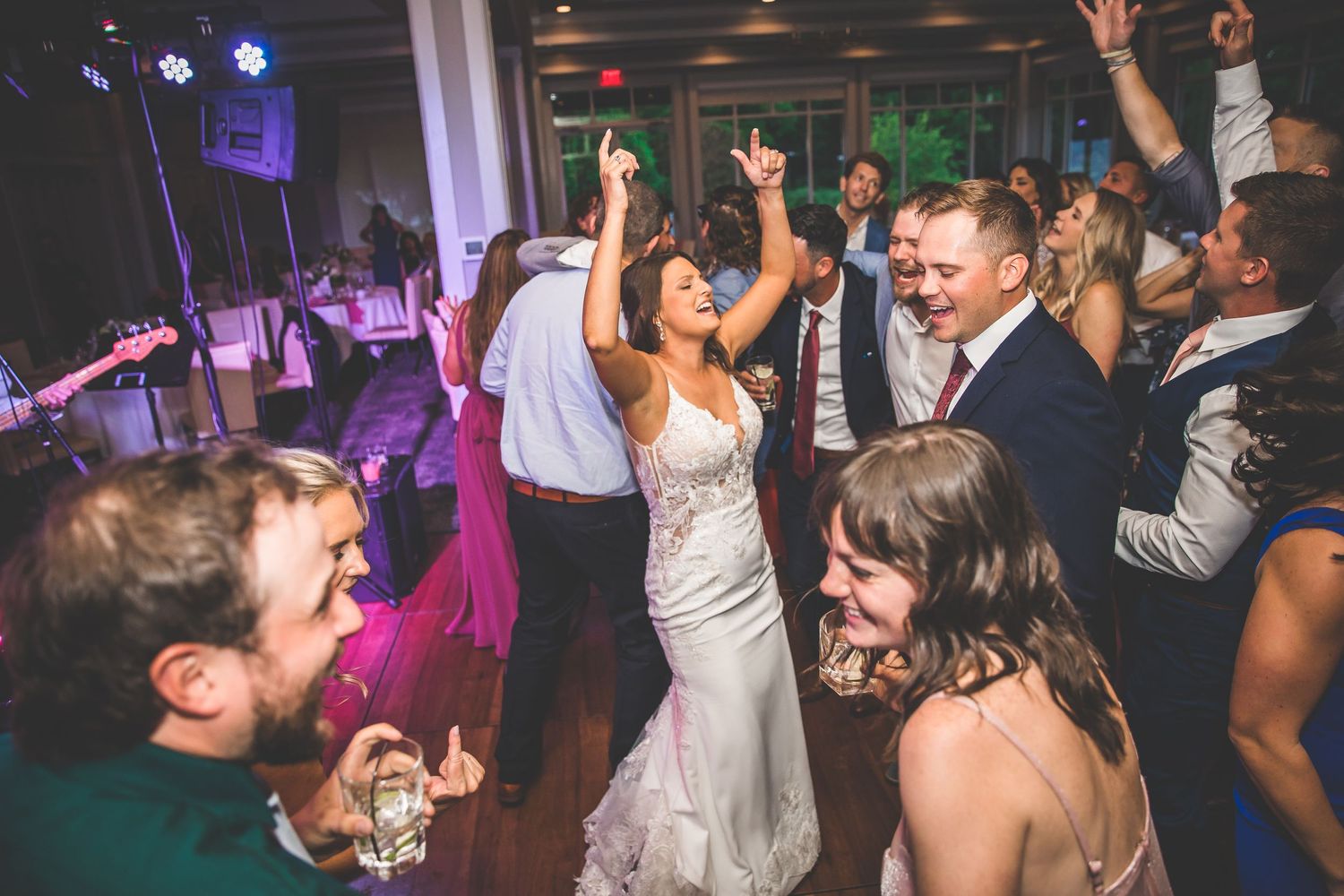 Festive wedding reception dance floor filled with guests celebrating under colored lights.