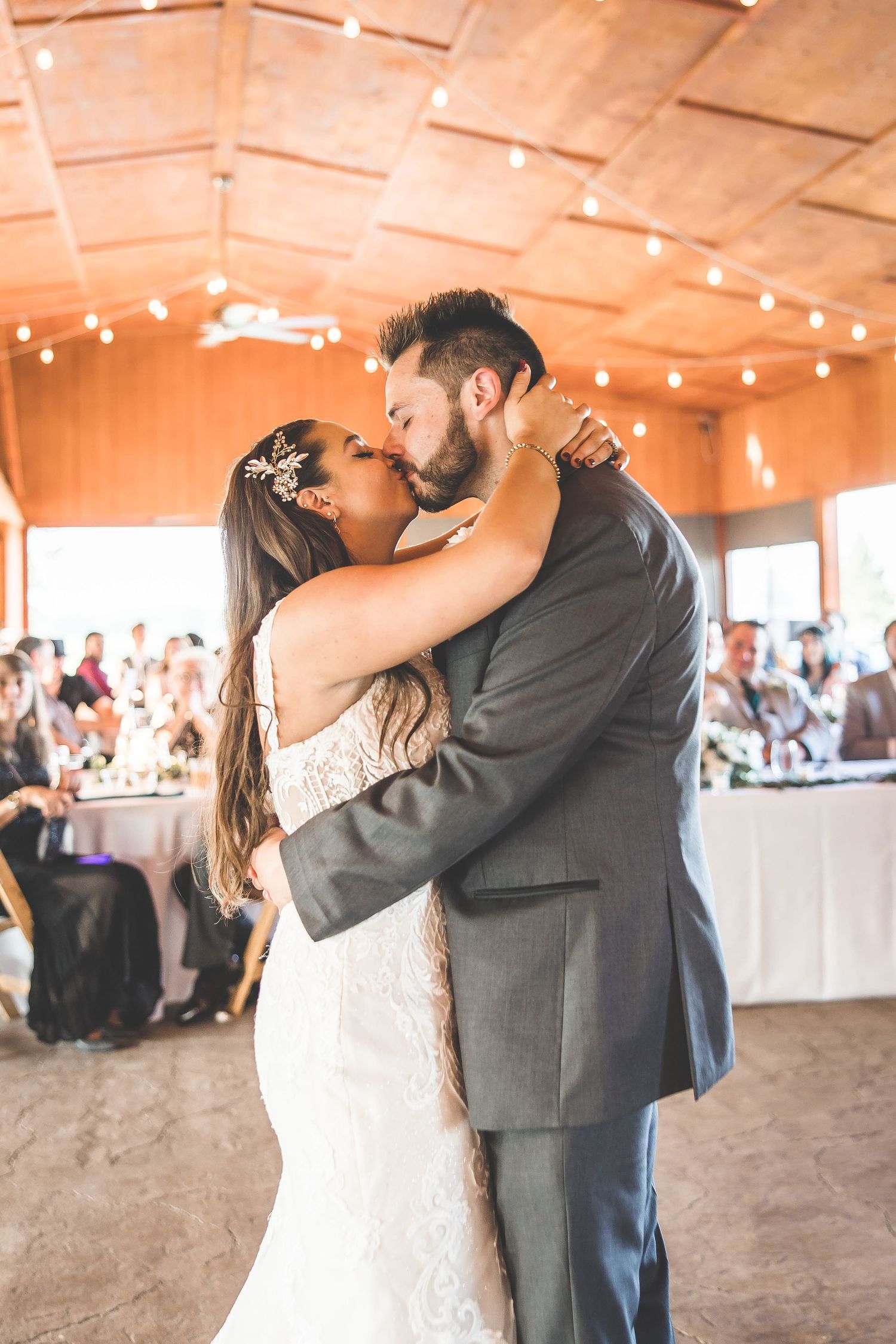 Wedding couple's romantic first dance in rustic venue decorated with string lights.