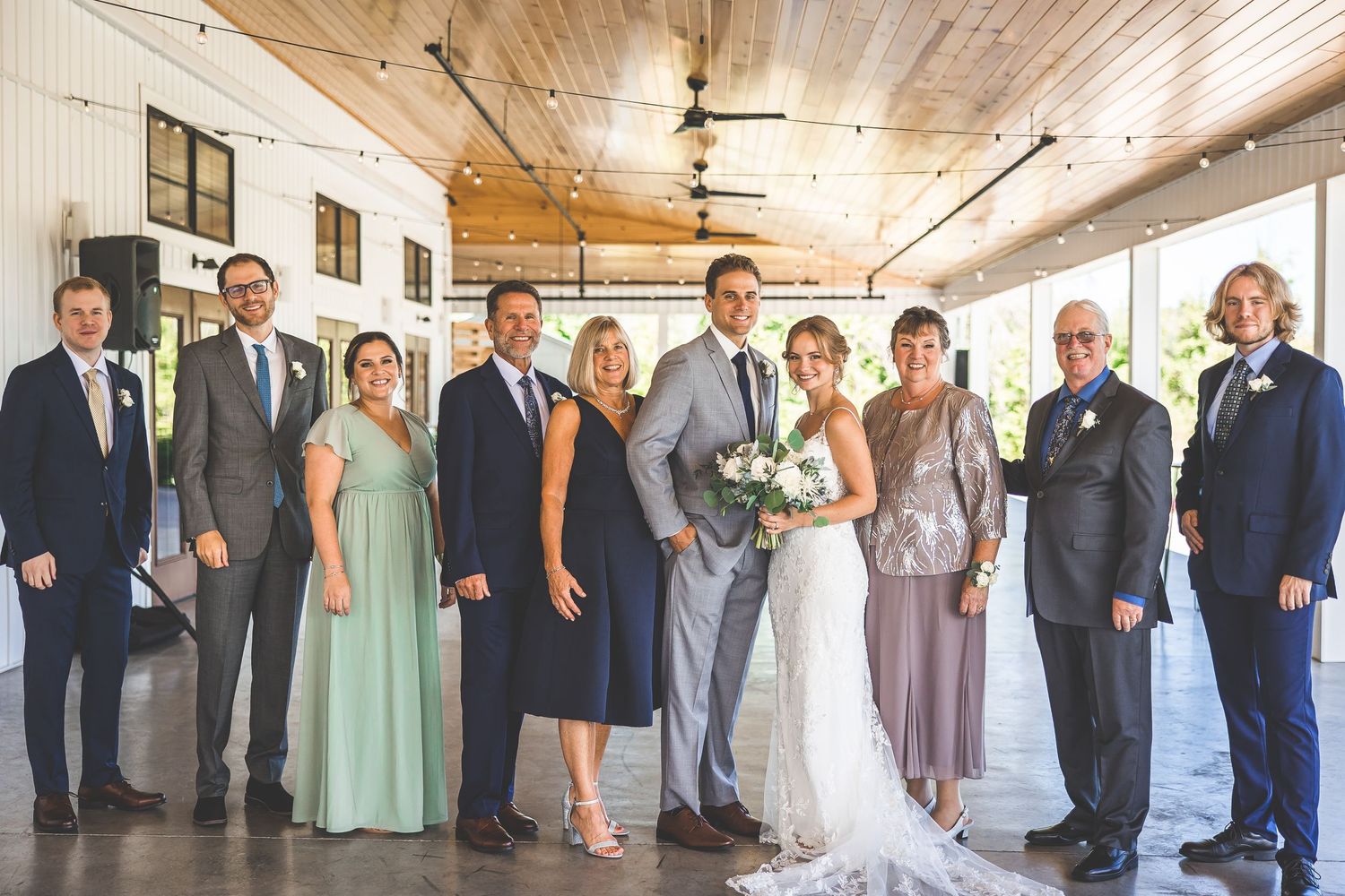 Wedding party members line up against a rustic wooden wall for formal photos.