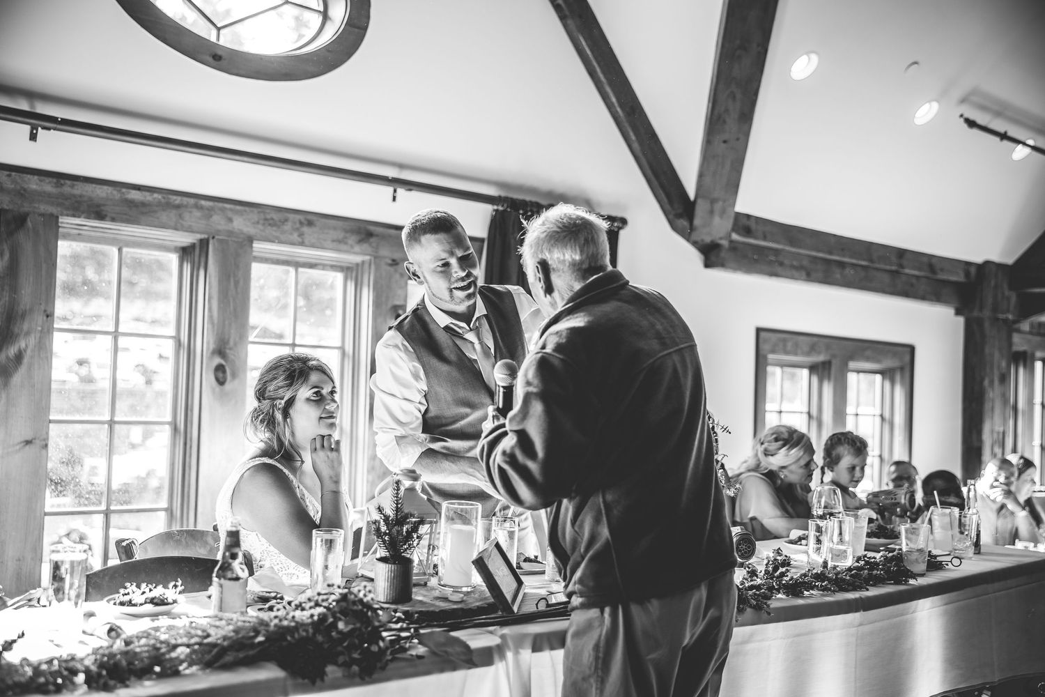 Wedding reception venue with rustic wooden beams and large windows letting in natural light.