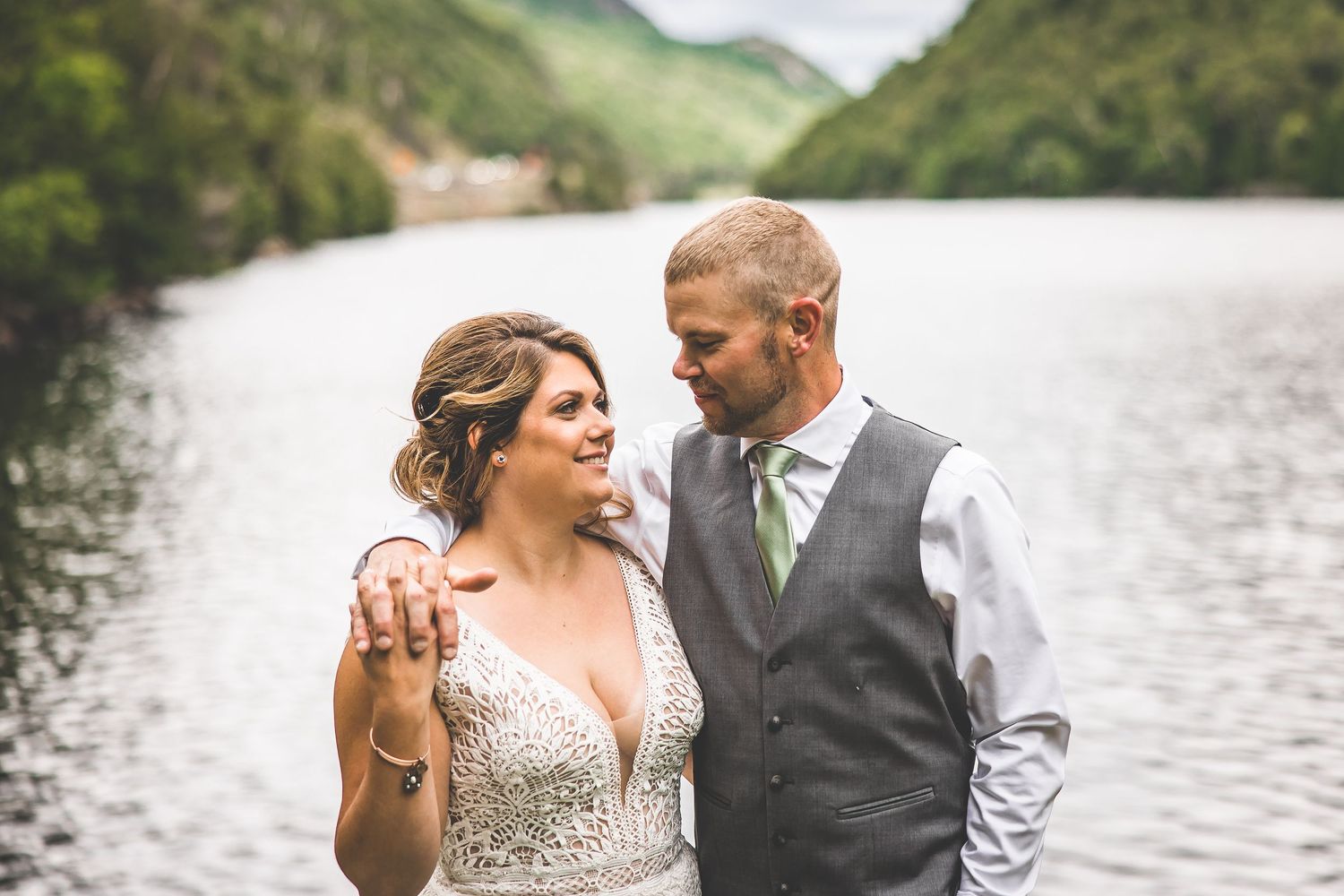 A romantic wedding portrait by a scenic lake with mountains in the background.