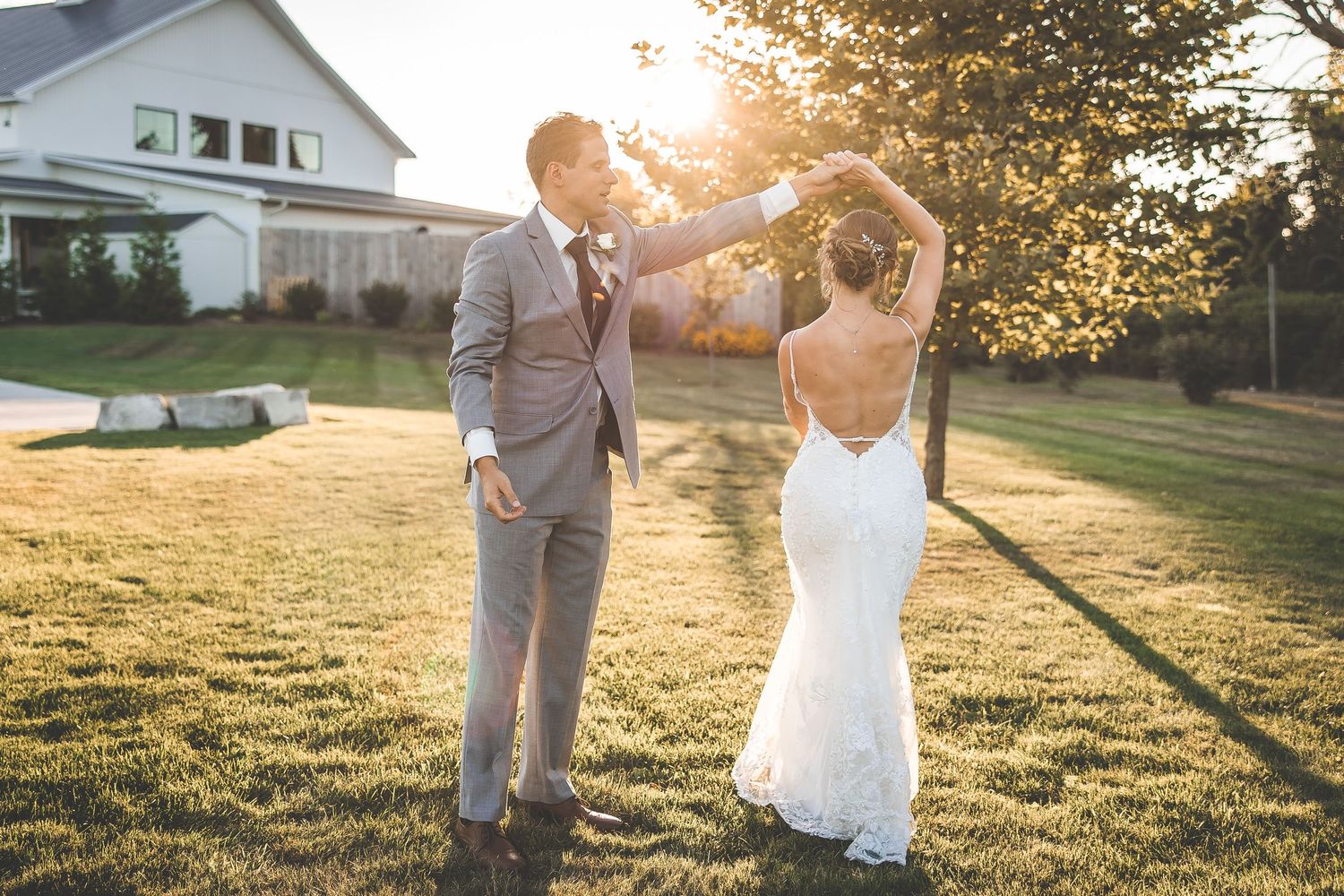 A couple dances together on a lawn at sunset with a house in the background.