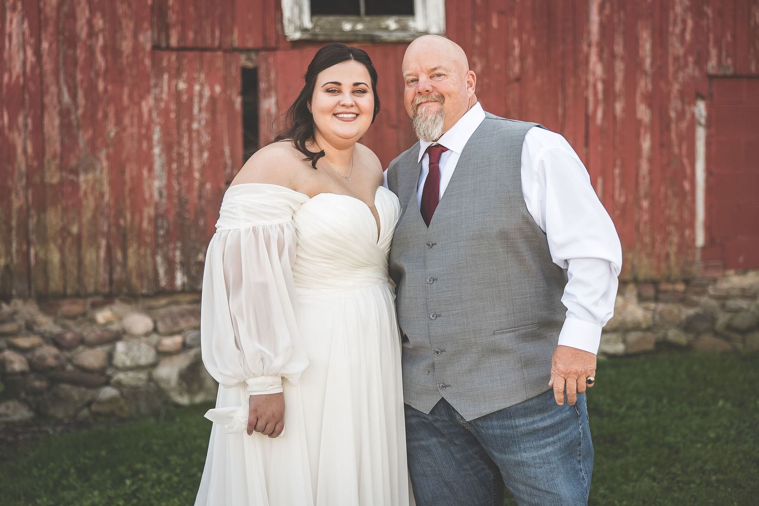 Couple poses for romantic wedding photos against a rustic red barn backdrop.