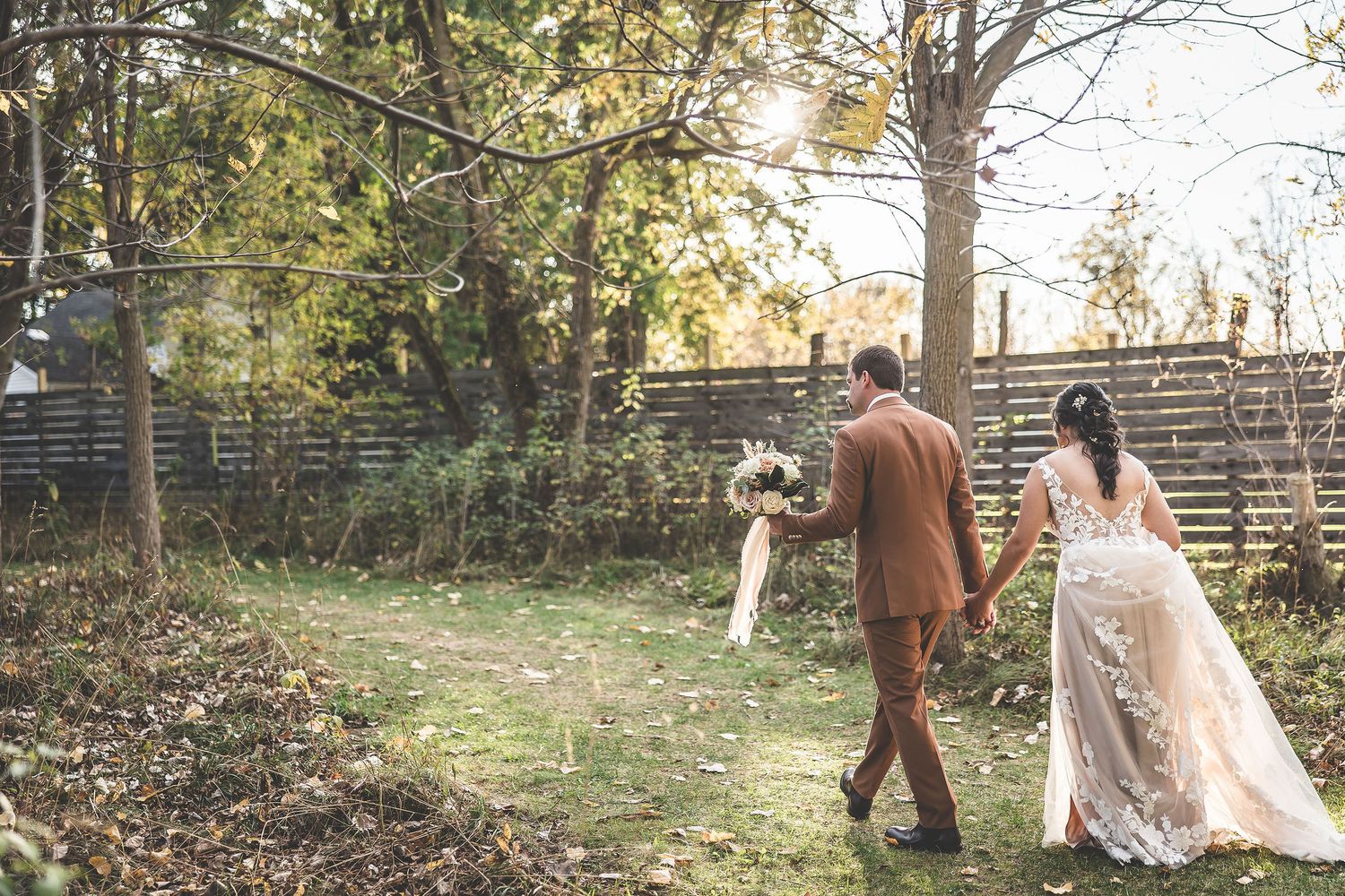 Wide landscape view of wedding couple walking through an autumn forest setting.