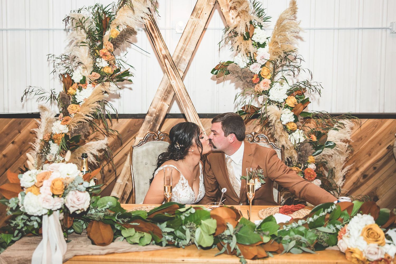 Wedding reception decor with white floral arrangements and rustic teepee-style backdrop.